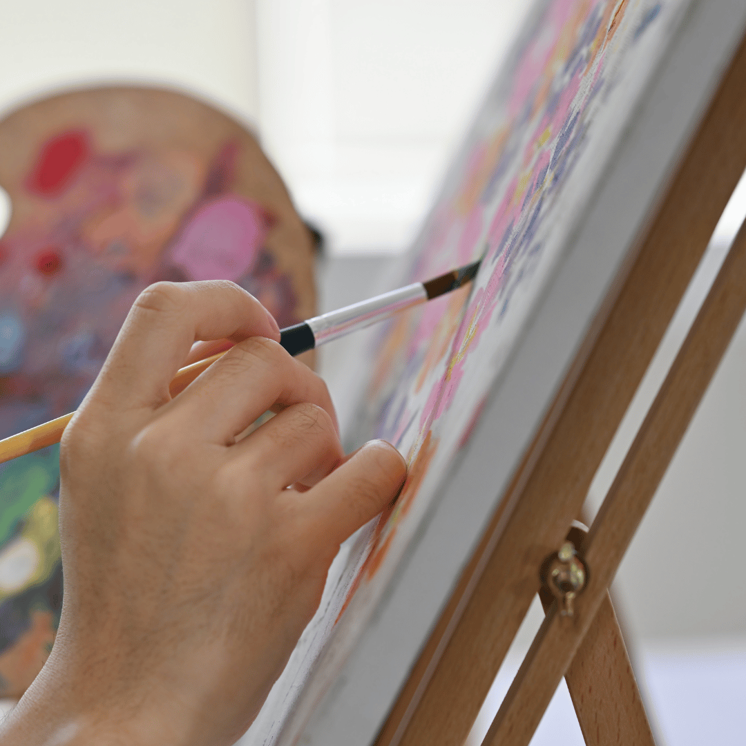 photograph from side of a hand holding brush painting on canvas