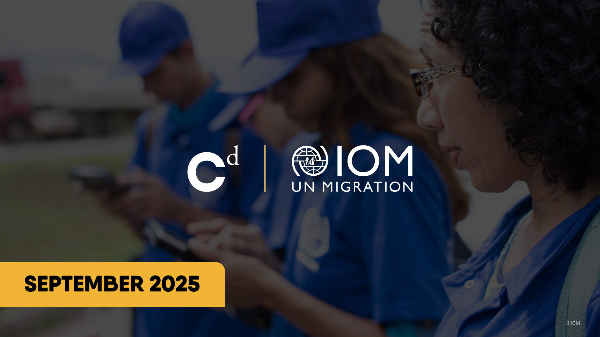 Group of people in blue uniforms looking at their phones, with IOM UN Migration logo and September 2025 text overlay.