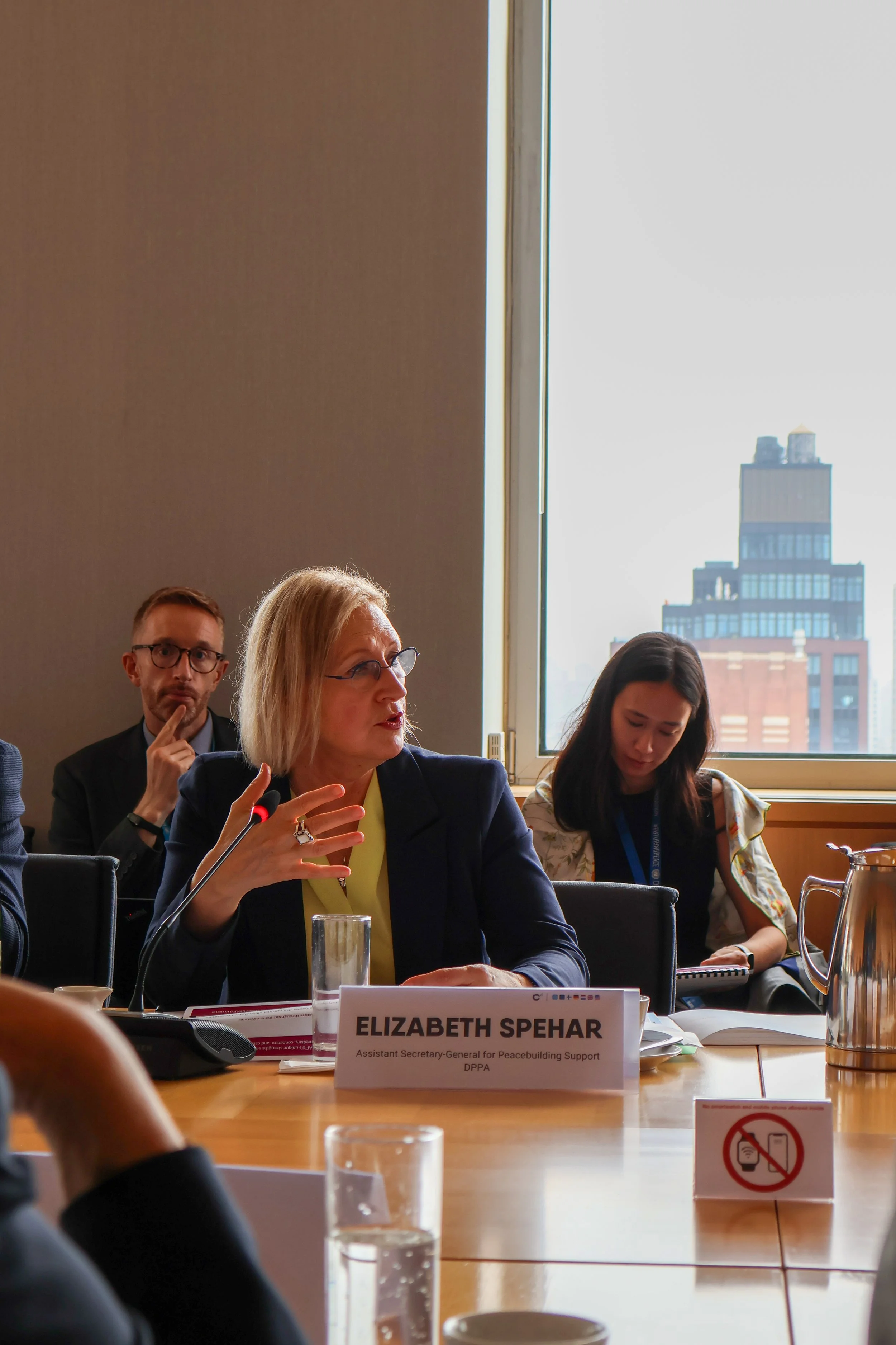 Elizabeth Spehar, Assistant Secretary-General for Peacebuilding Support, speaks during a meeting in a conference room with a cityscape visible through the window.