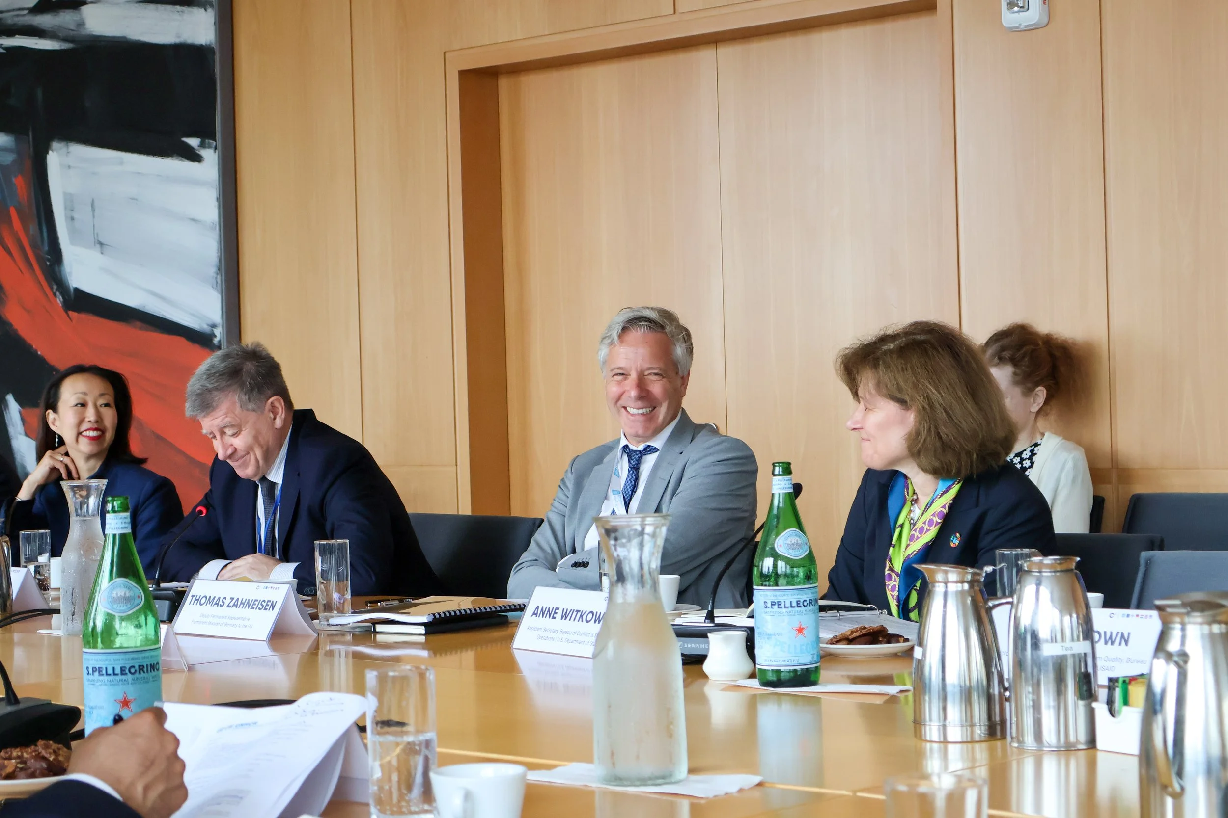 A group of professionals at a meeting table, smiling and engaging, with water bottles and documents in front of them.