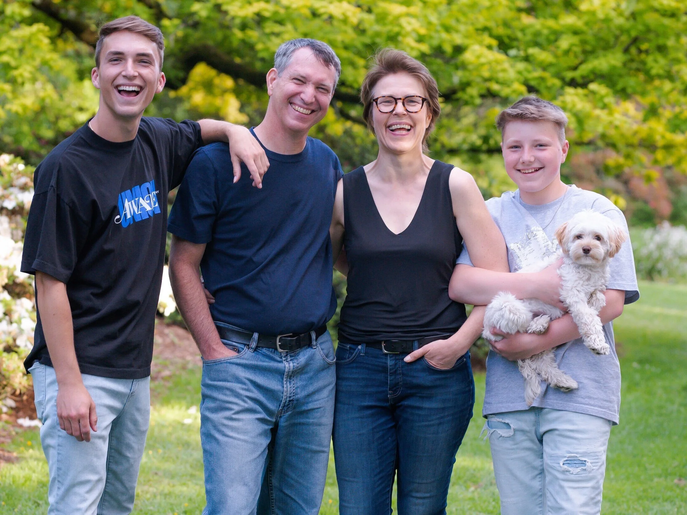 Brynnen Ford, Ph.D with her husband and two sons standing outdoors with a small white dog, smiling and enjoying a sunny day in a green park.
