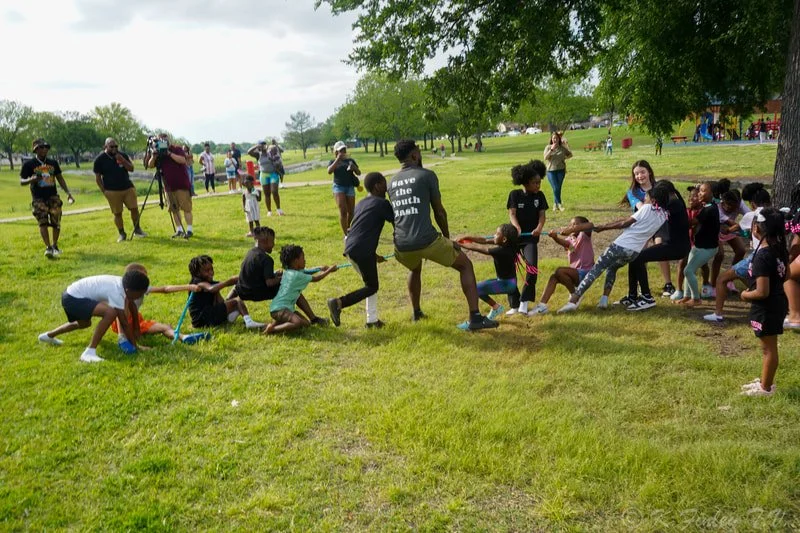 Children and adults playing a game of tug-of-war in a park on a cloudy day.