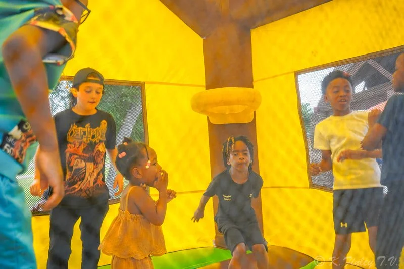 Children playing inside a yellow bounce house with mesh windows.