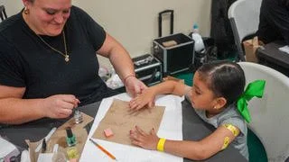 A young girl with a green bow in her hair getting a manicure from a woman.