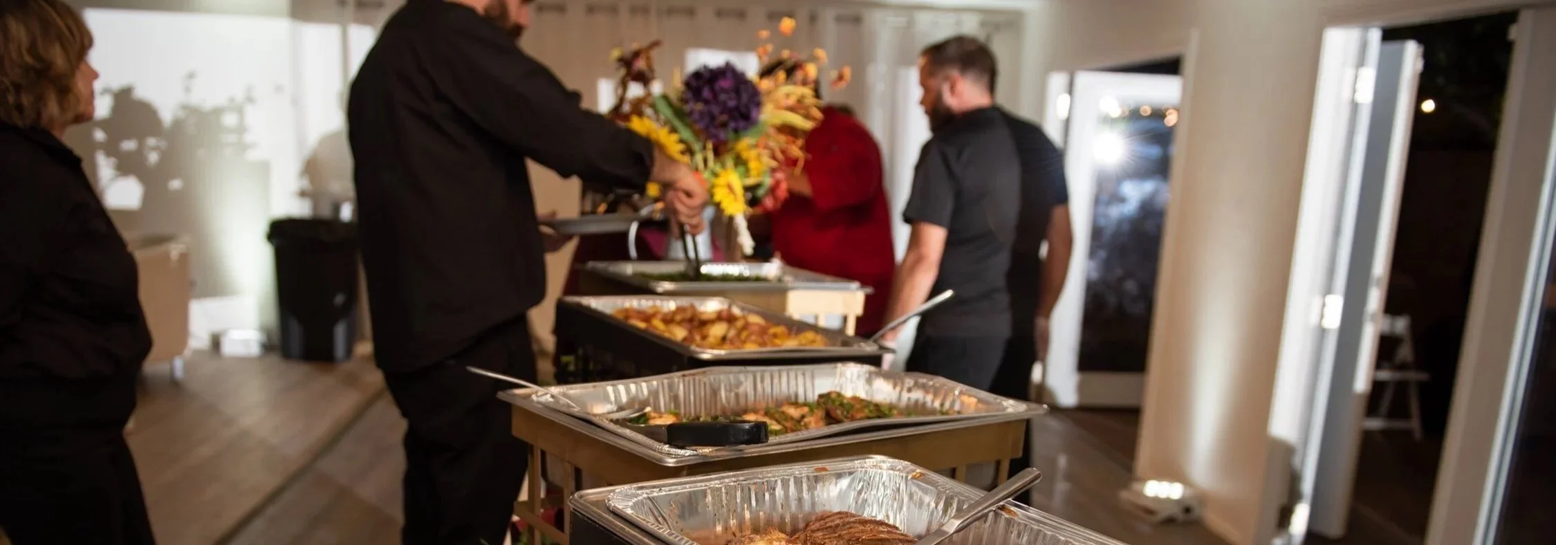 People serving food at a buffet table during a gathering.