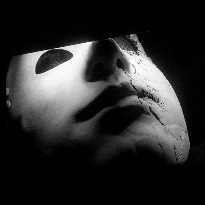 A black and white photo of a cracked mask resembling a human face.