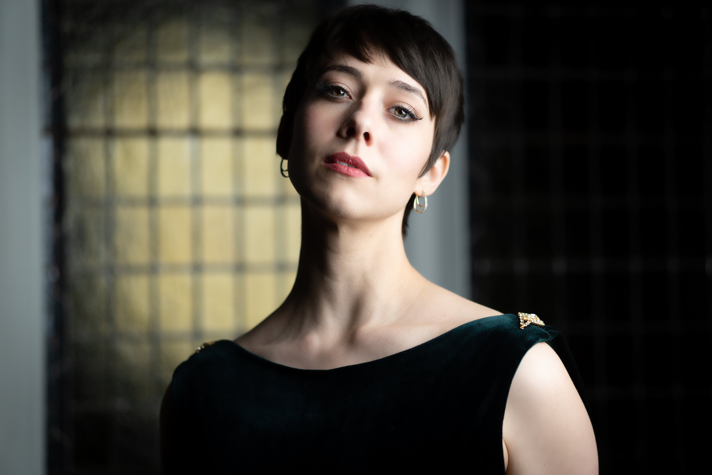 Portrait of a person with short hair wearing a dark sleeveless top, standing in front of a grid-patterned background.