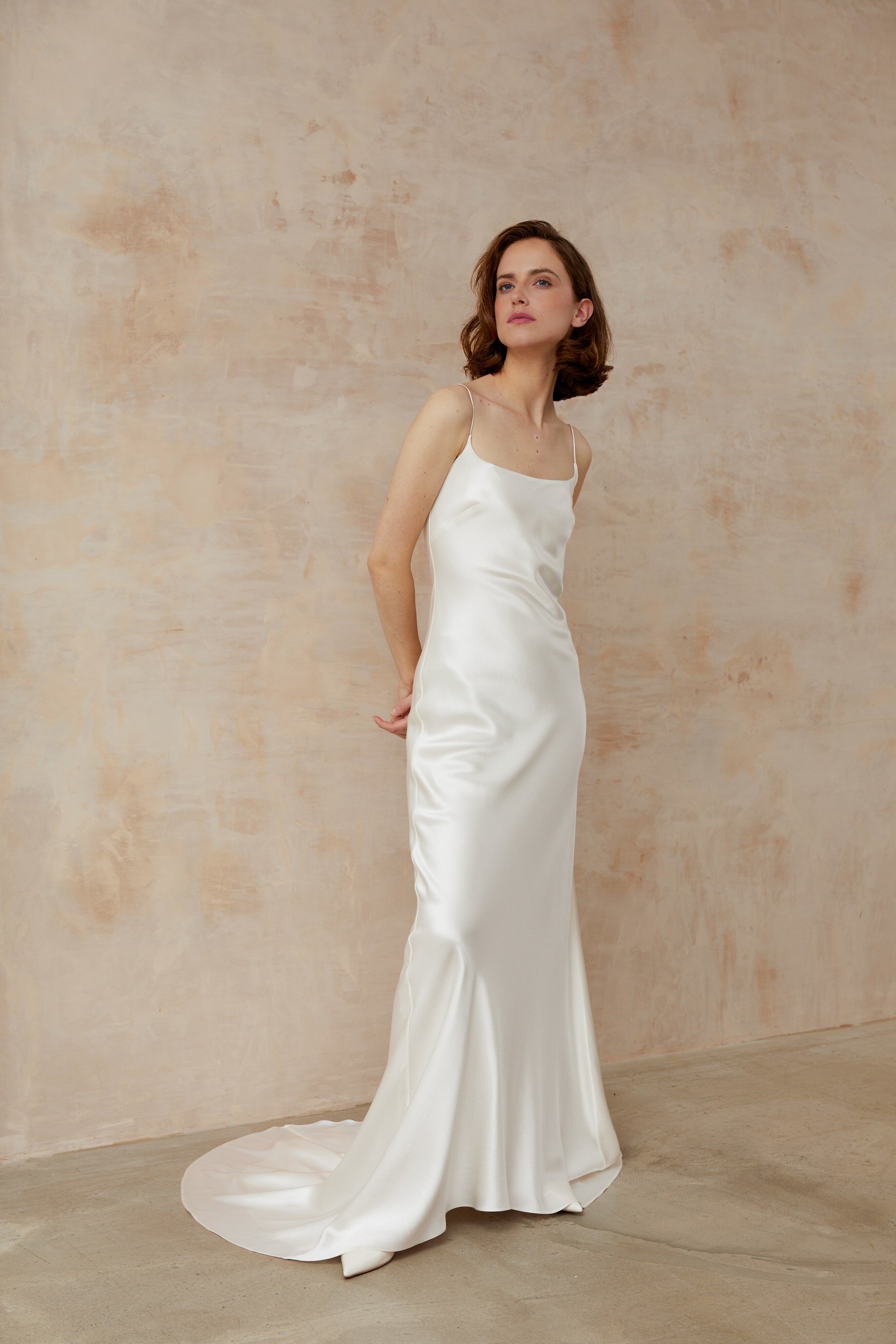 Sophisticated woman in a white dress with a square neck, standing against a pristine white wall.