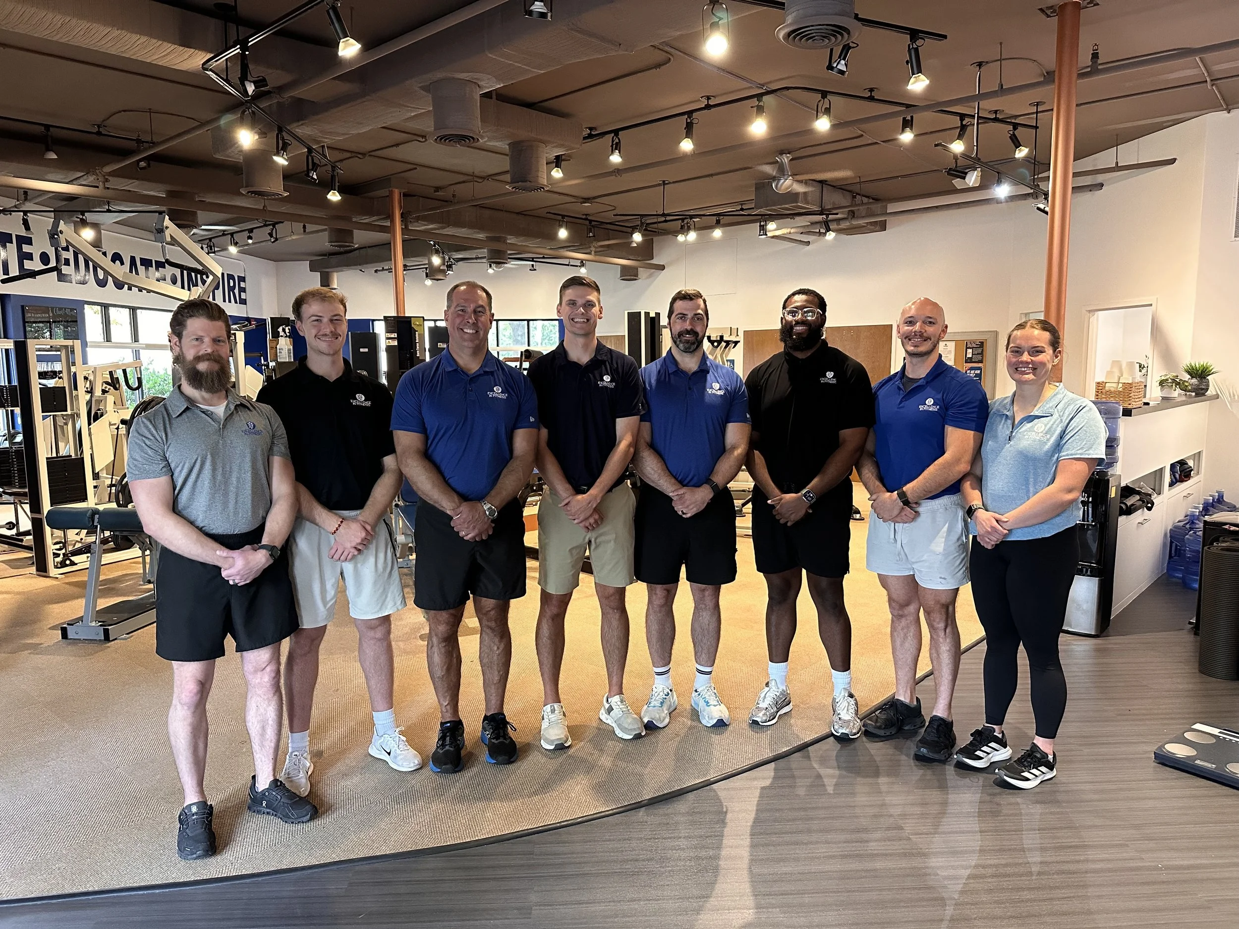 The Excellence In Fitness team standing together inside the private personal training studio in Annapolis, Maryland, smiling in front of strength training equipment.