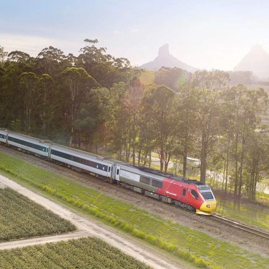 A red and yellow train with grey passenger carriages traveling through a green field.