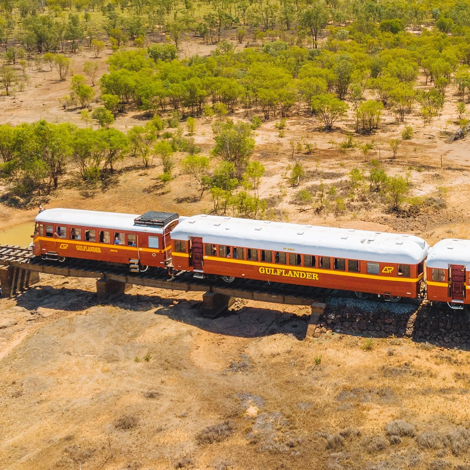 The vintage Gulflander train crossing a wooden bridge over a dry creek bed in the Australian outback.
