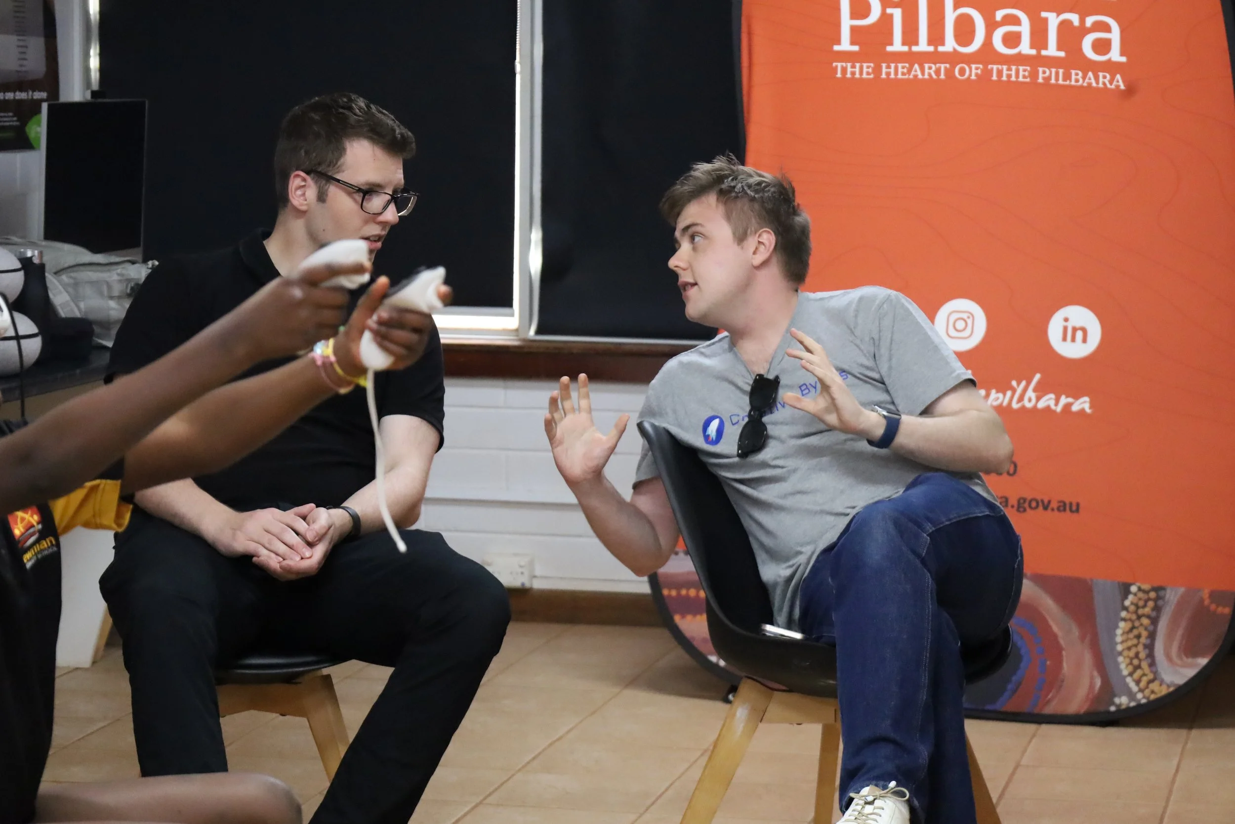 Two people standing in a modern room with a screen displaying 'Creative Byte: Creative Youth Coding', surrounded by tables and library shelves.