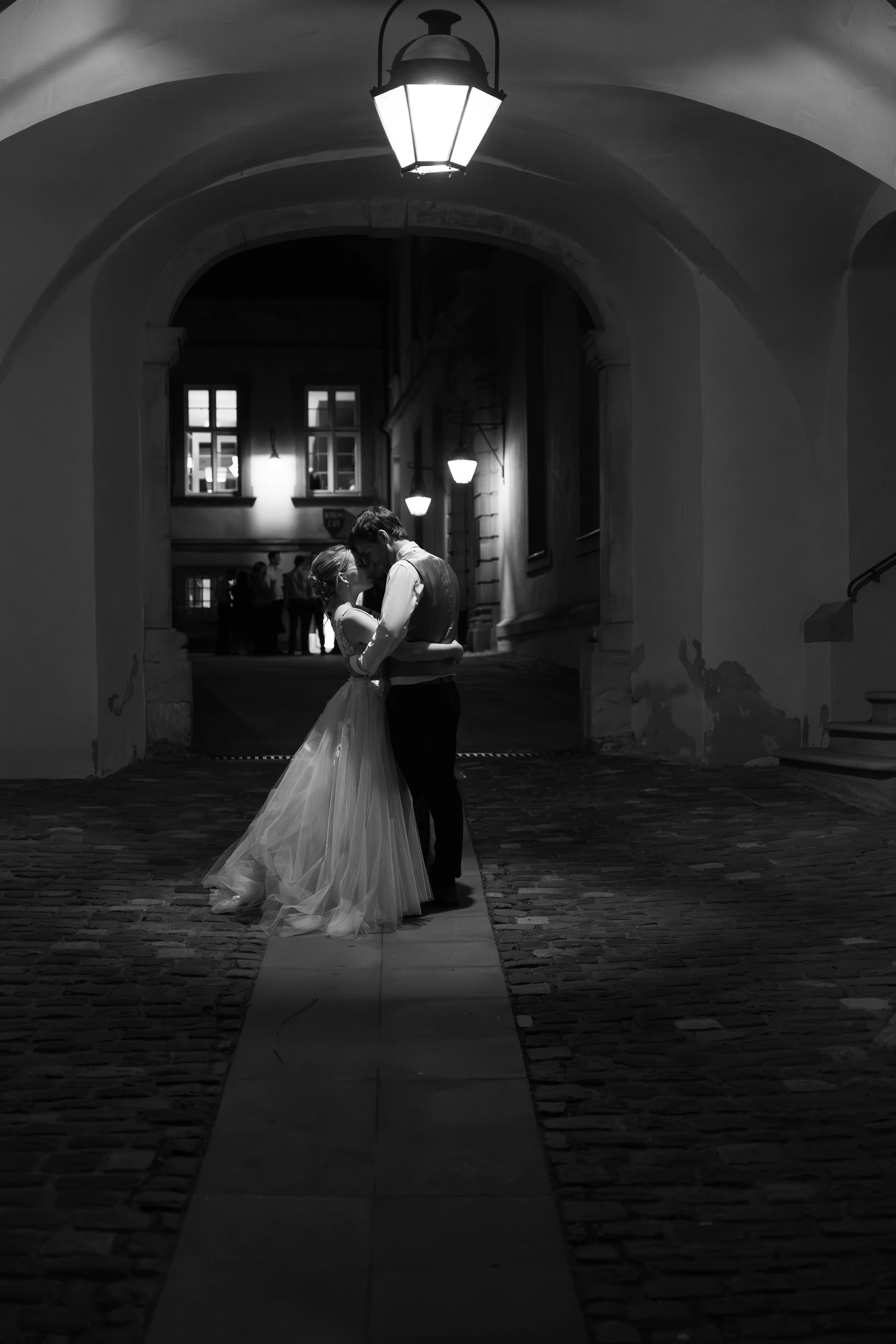 Brautpaarfoto bei Nacht in Schwarz Weiß. Brautpaar steht unter einer Lampe in einem historischen Torbogen und schmiegt die Köpfe aneinander