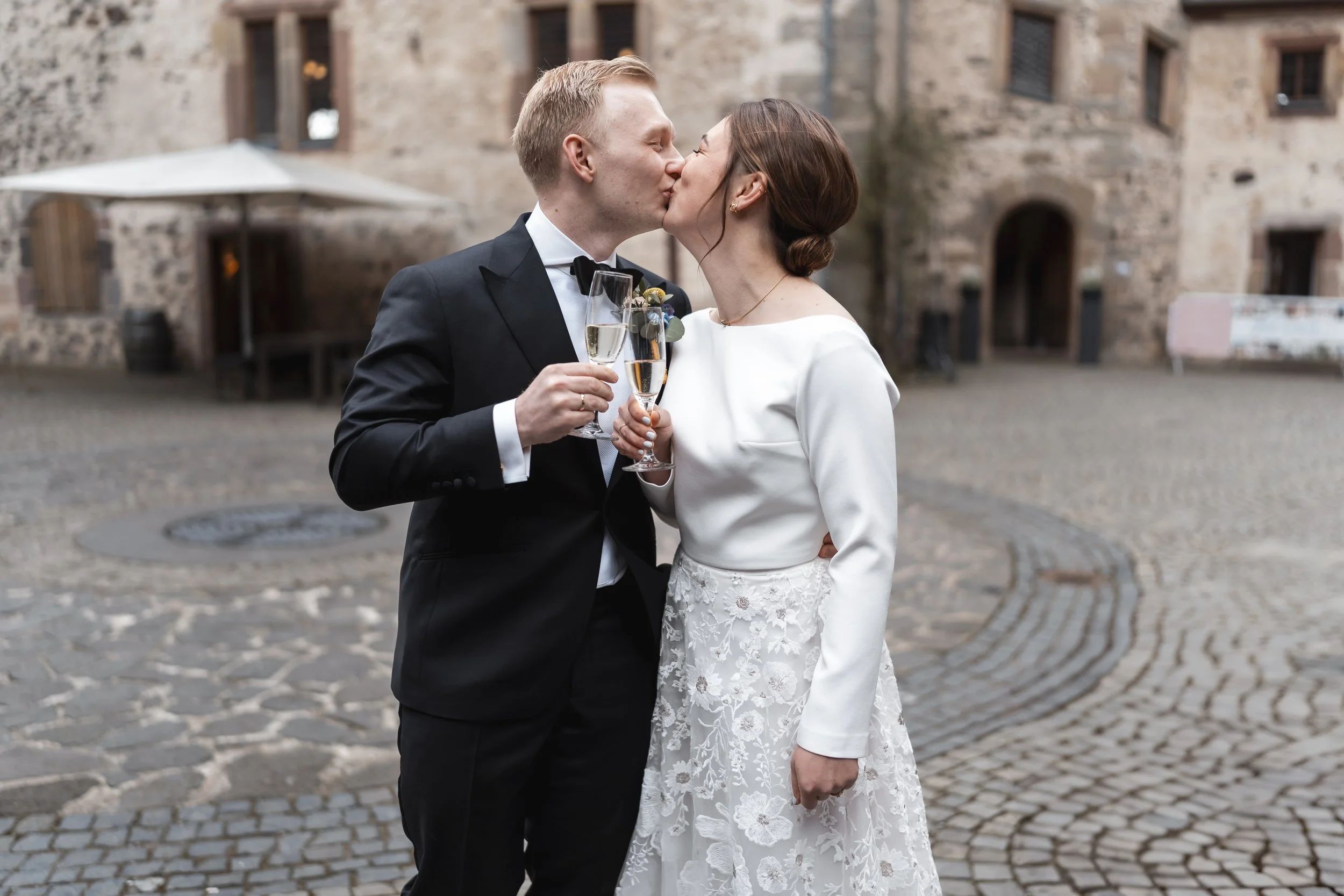Brautpaar küsst sich und stößt bei Sektempfang im Burghof von Schloss Romrod an