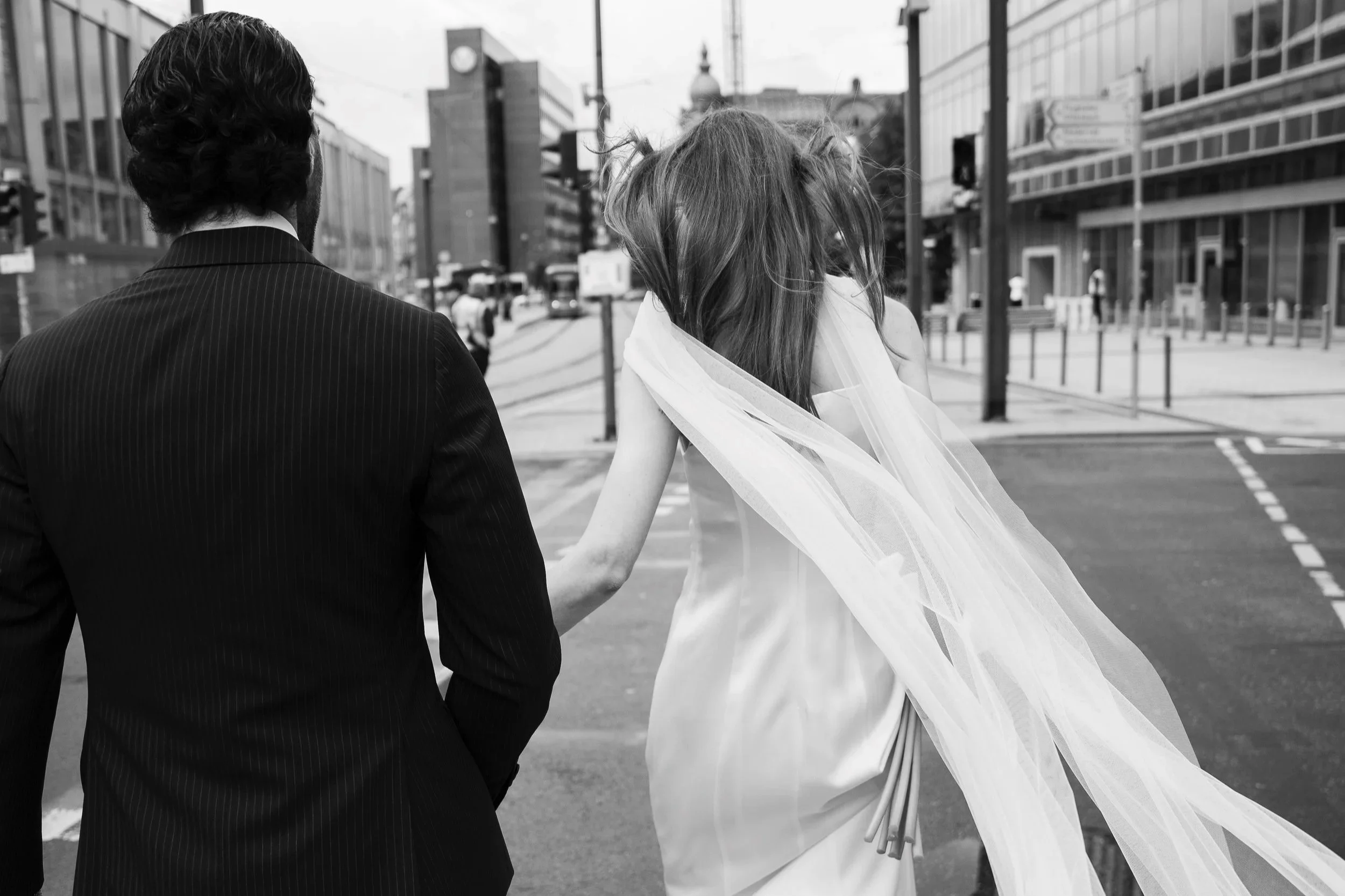 Brautpaar auf dem Weg zur Hochzeit im Standesamt Römer in Frankfurt von hinten fotografiert mit wehendem Schleier