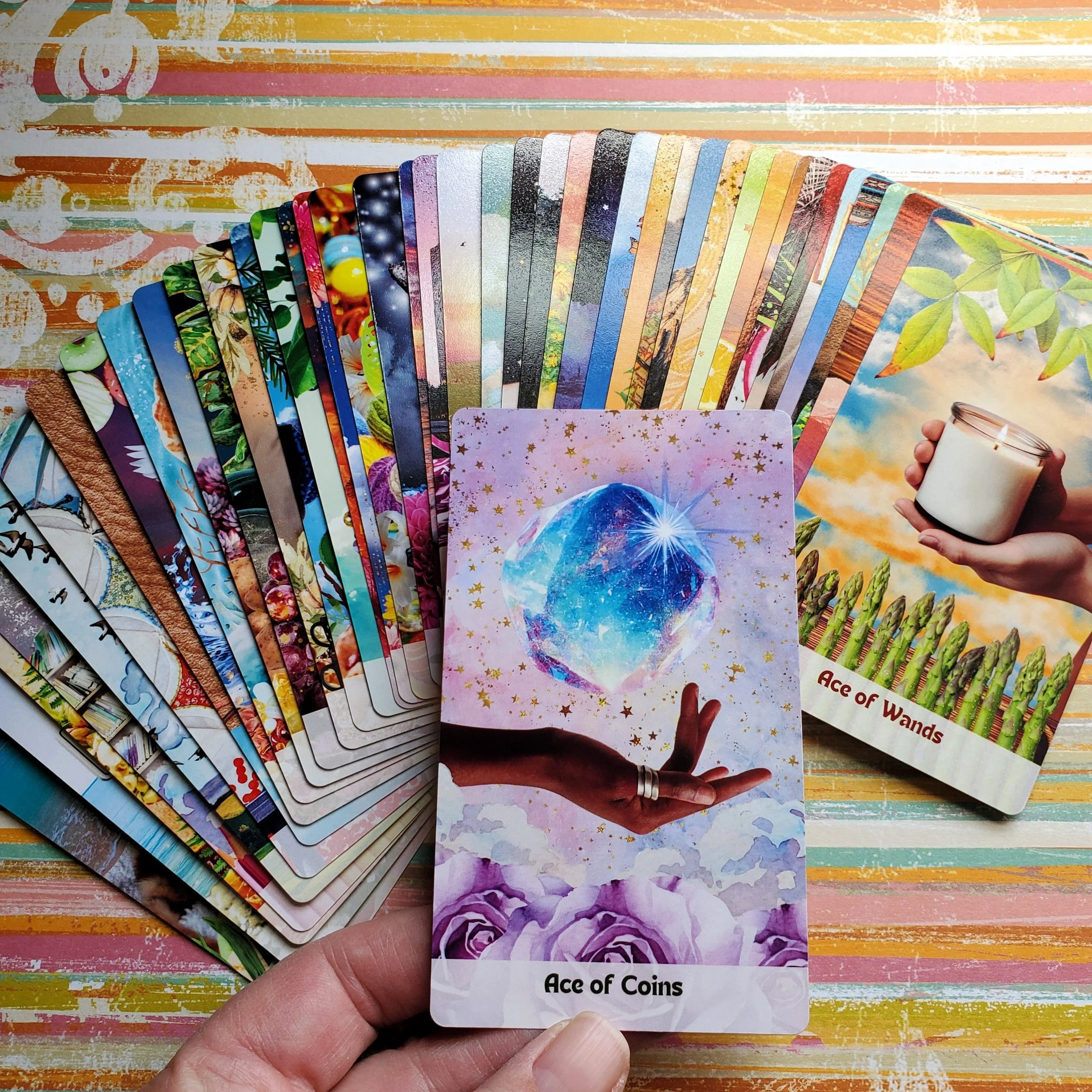 How Did I Get Here Tarot deck fanned out showing colorful collage imagery and hand holding Ace of Coins card — pop art collage indie tarot deck by S.G. Stasi Designs