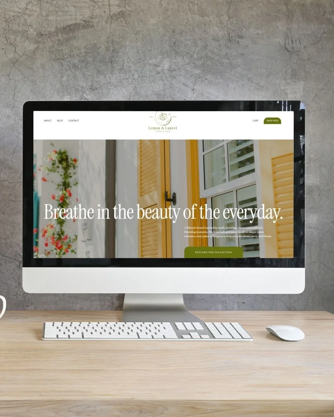 Dell iMac computer on a wooden desk displaying a website for Lemon & Laurel, a lifestyle brand, against a concrete wall background.