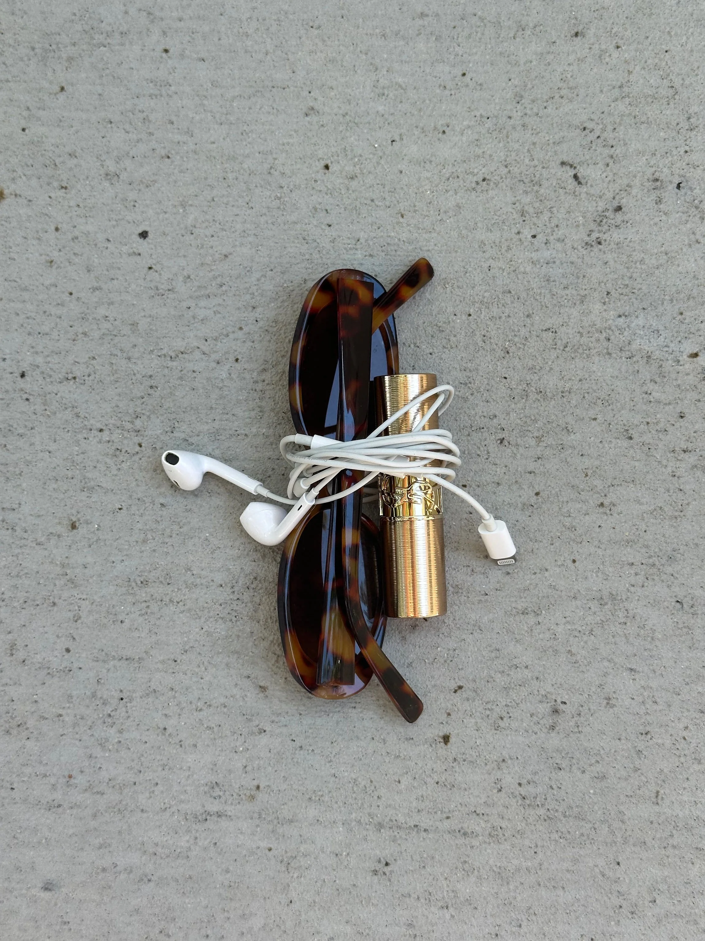 sunglasses and lipstick wrapped in headphones on a counter
