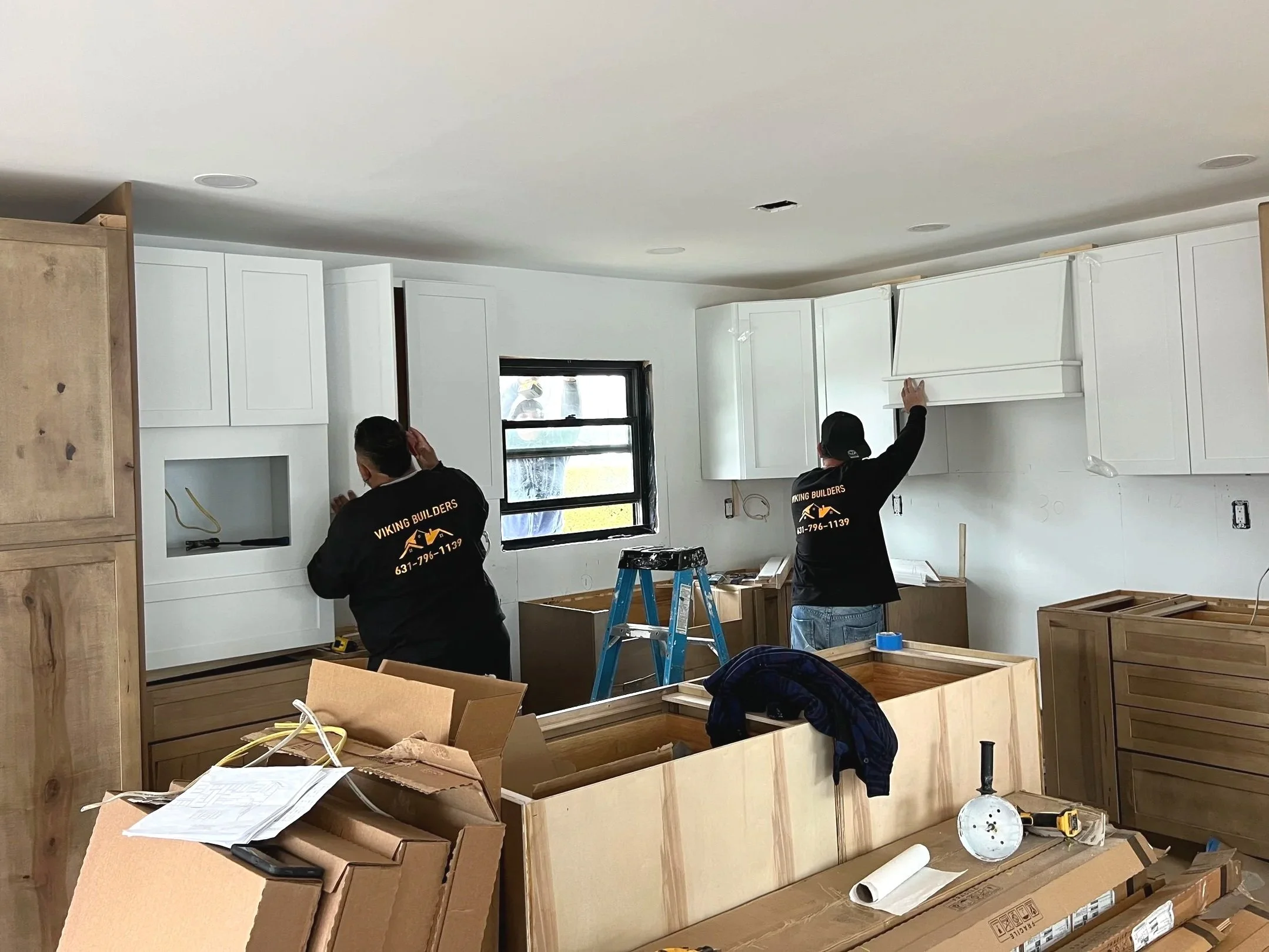 Modern bathroom with glass shower, dual-sink vanity, large mirror, white countertops, and wooden accents. Towels hang near the toilet, and decorative shelves with plants adorn the wall.