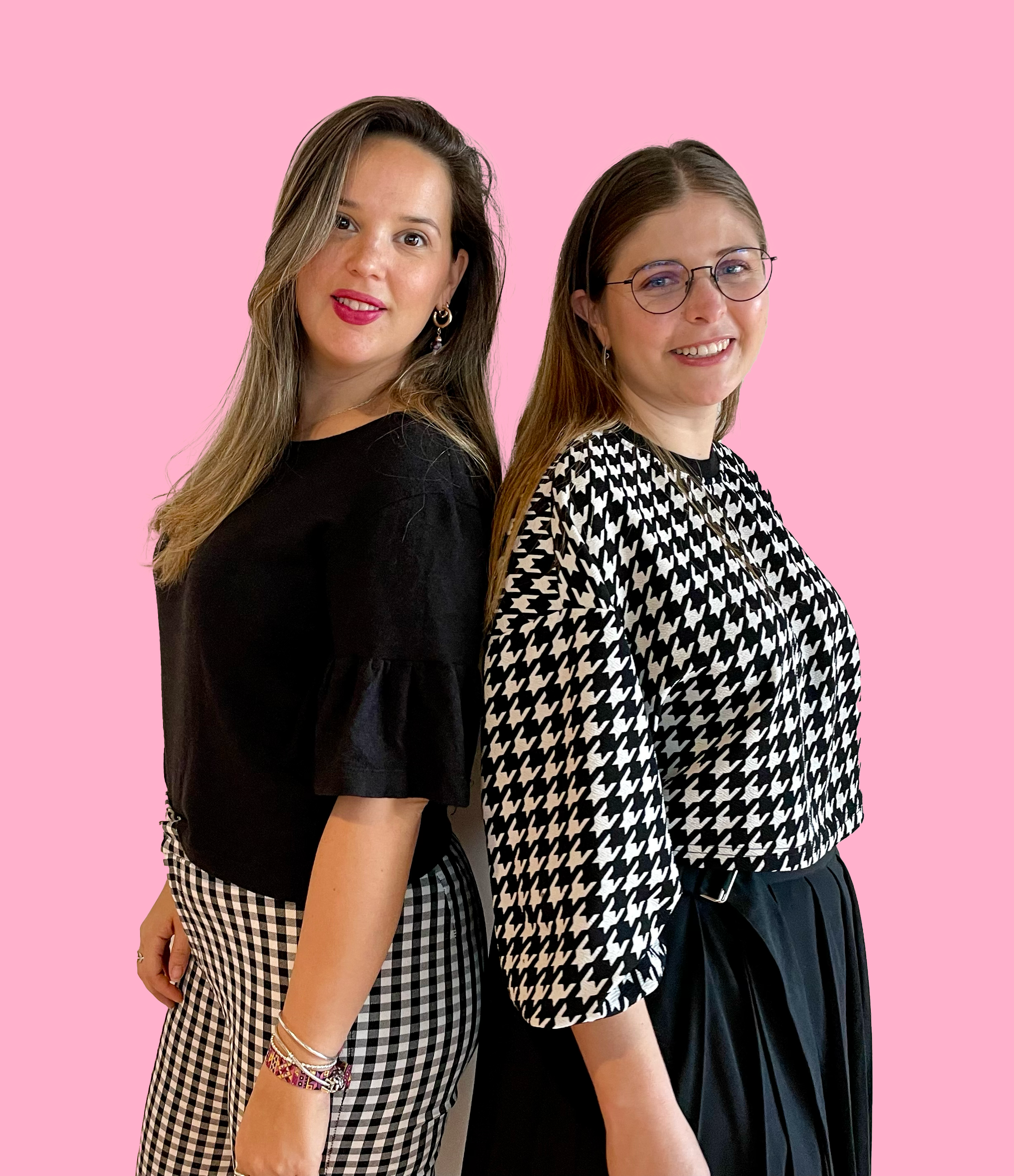 Two women standing back-to-back against a pink background, smiling at the camera.