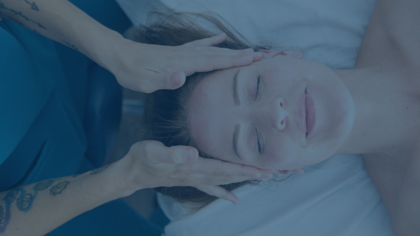 A woman receiving a gentle massage or therapy on her forehead and temples from a therapist in a clinical or wellness setting.