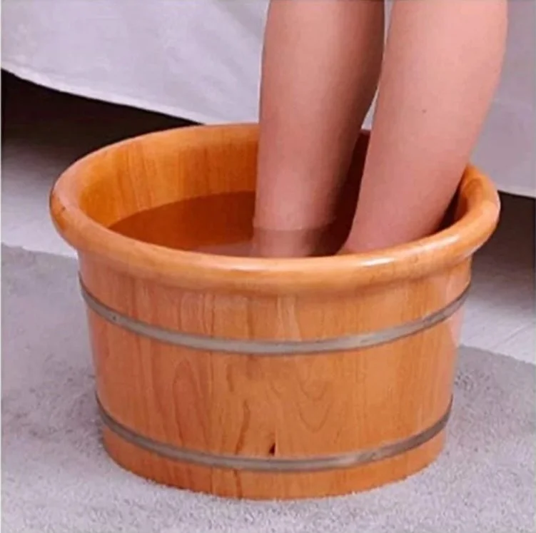 Person's legs soaking in a wooden foot spa filled with water.