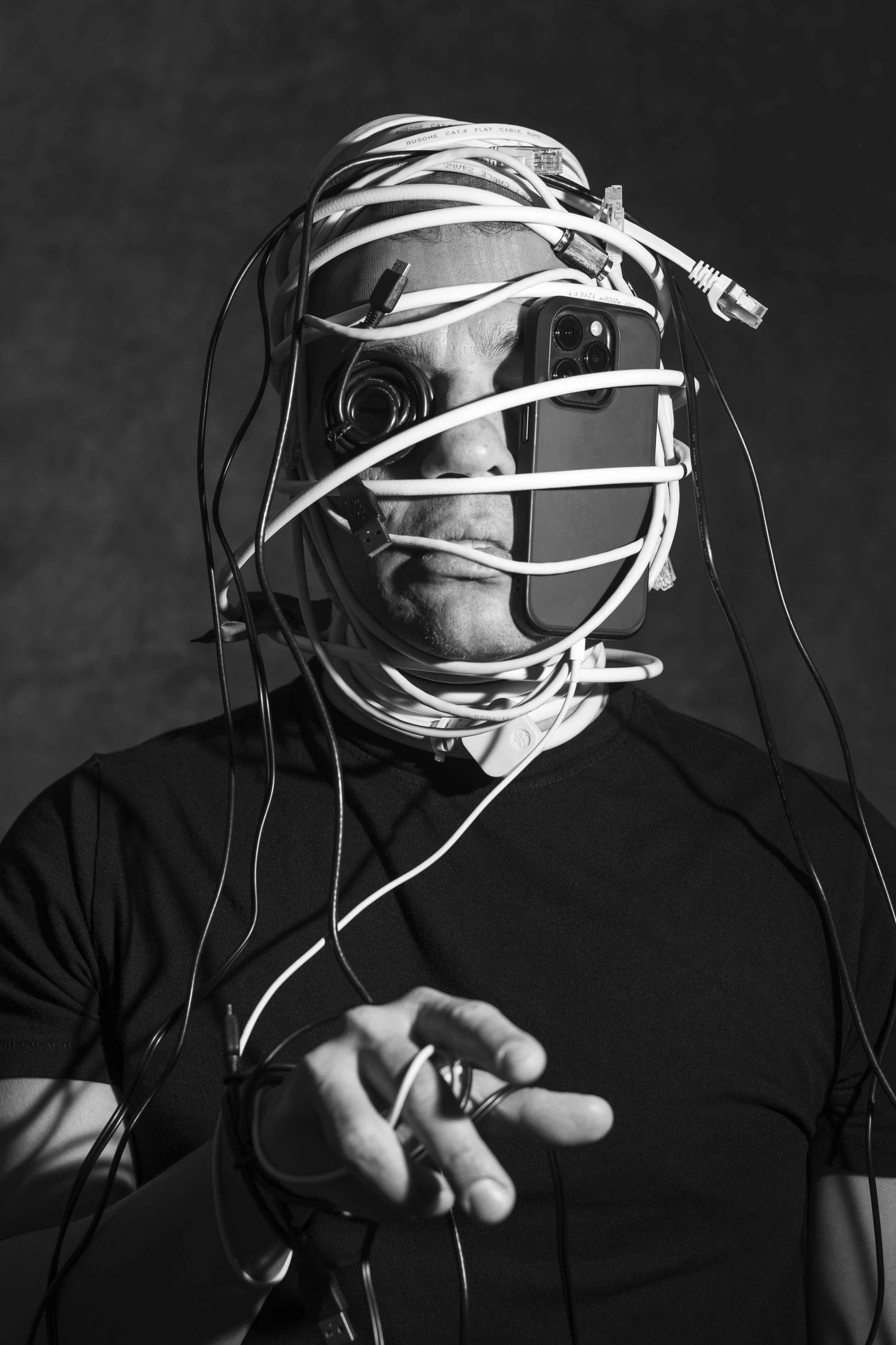 Person wrapped in cables with electronic devices, black and white photo