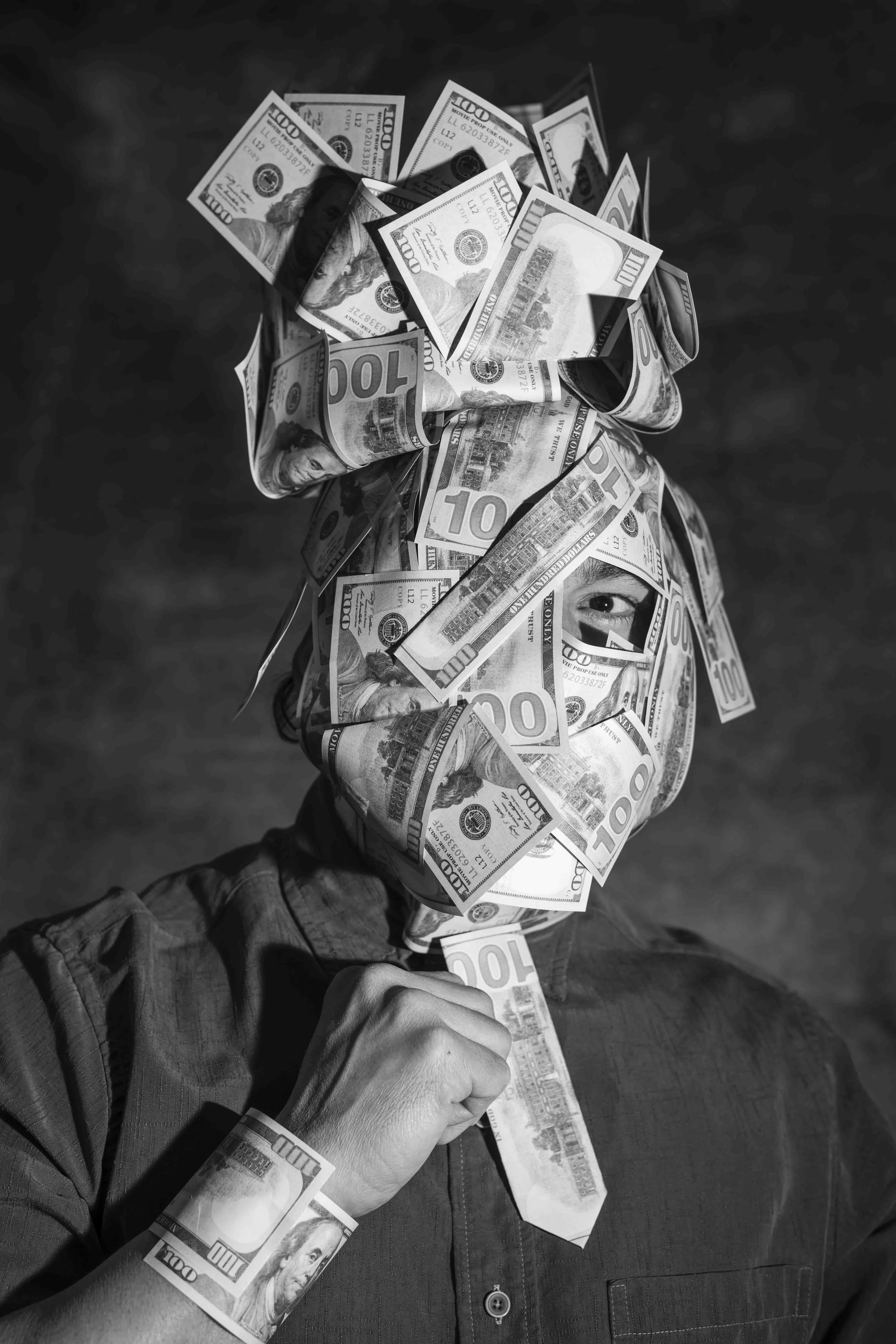 Person with face and head covered in taped hundred-dollar bills, wearing a collared shirt, black and white image.