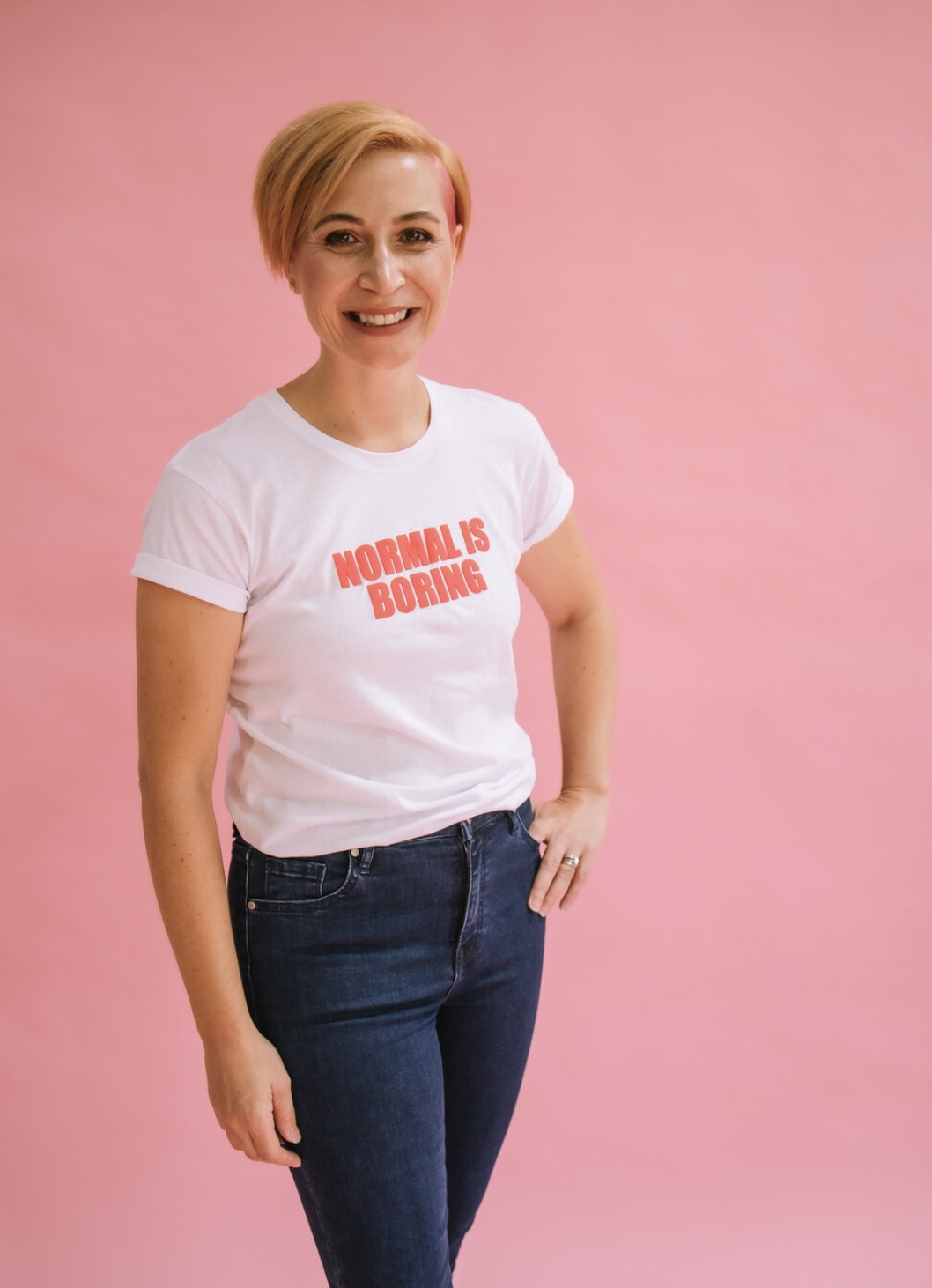 Person in a white t-shirt with "Normal is Boring" text, standing against a pink background.
