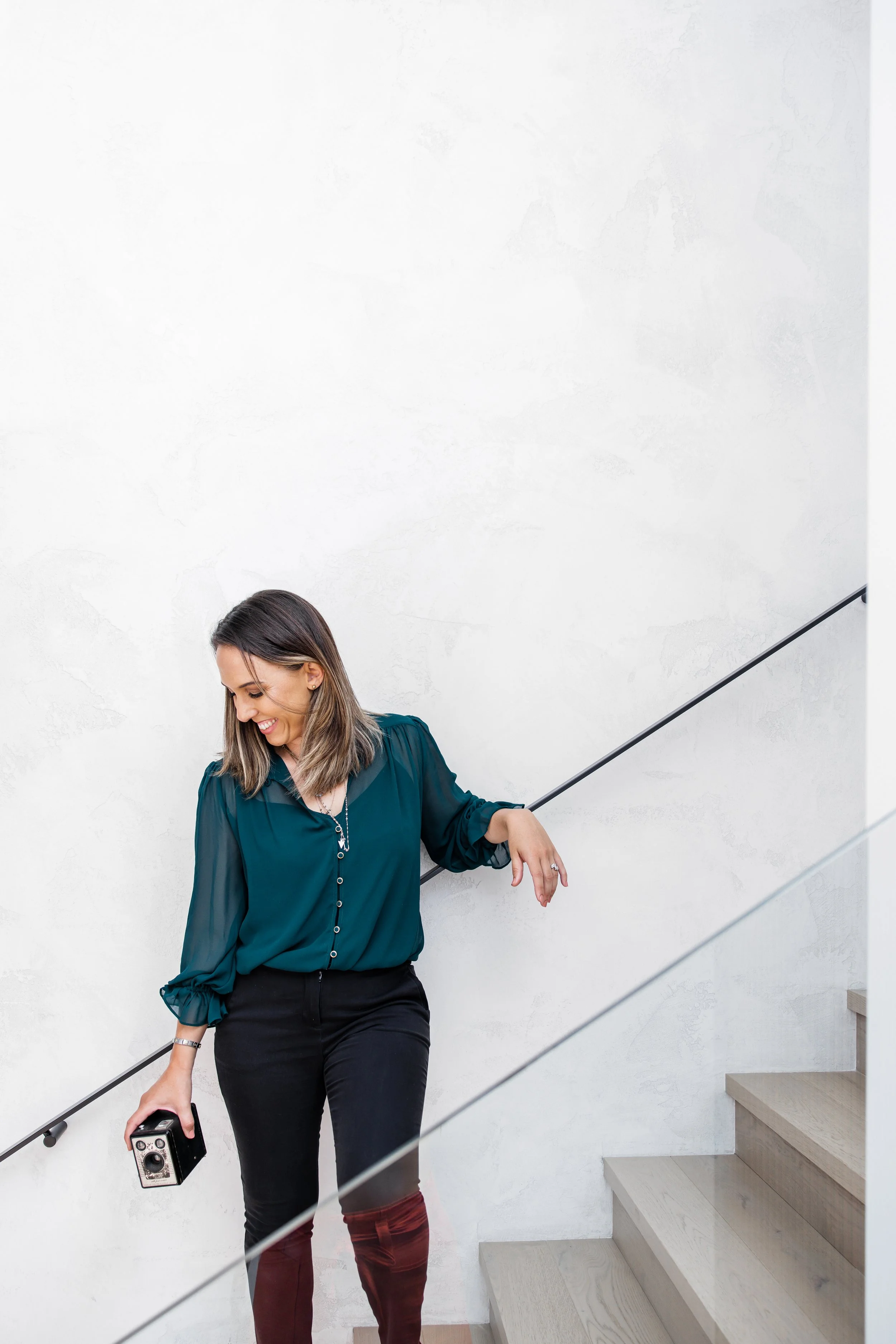 Woman in a green blouse holding a vintage camera, standing on stairs with a white background.