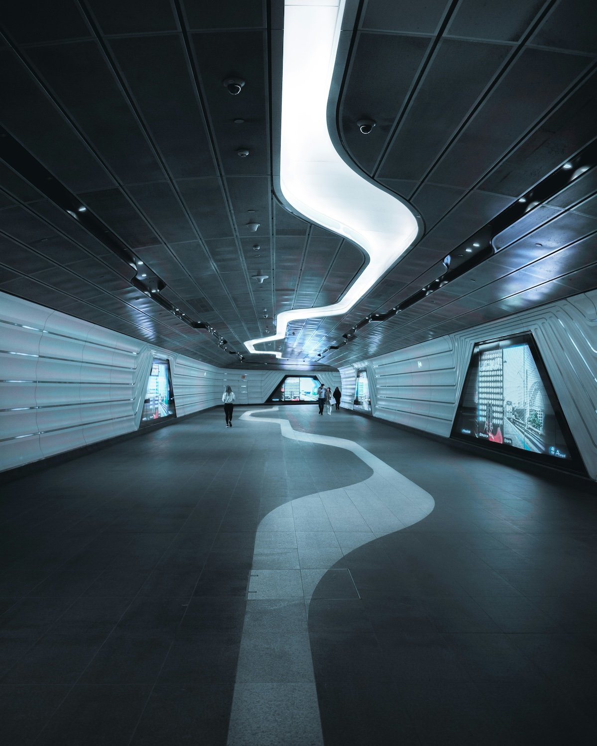 Modern underground walkway with curved ceiling light and digital displays