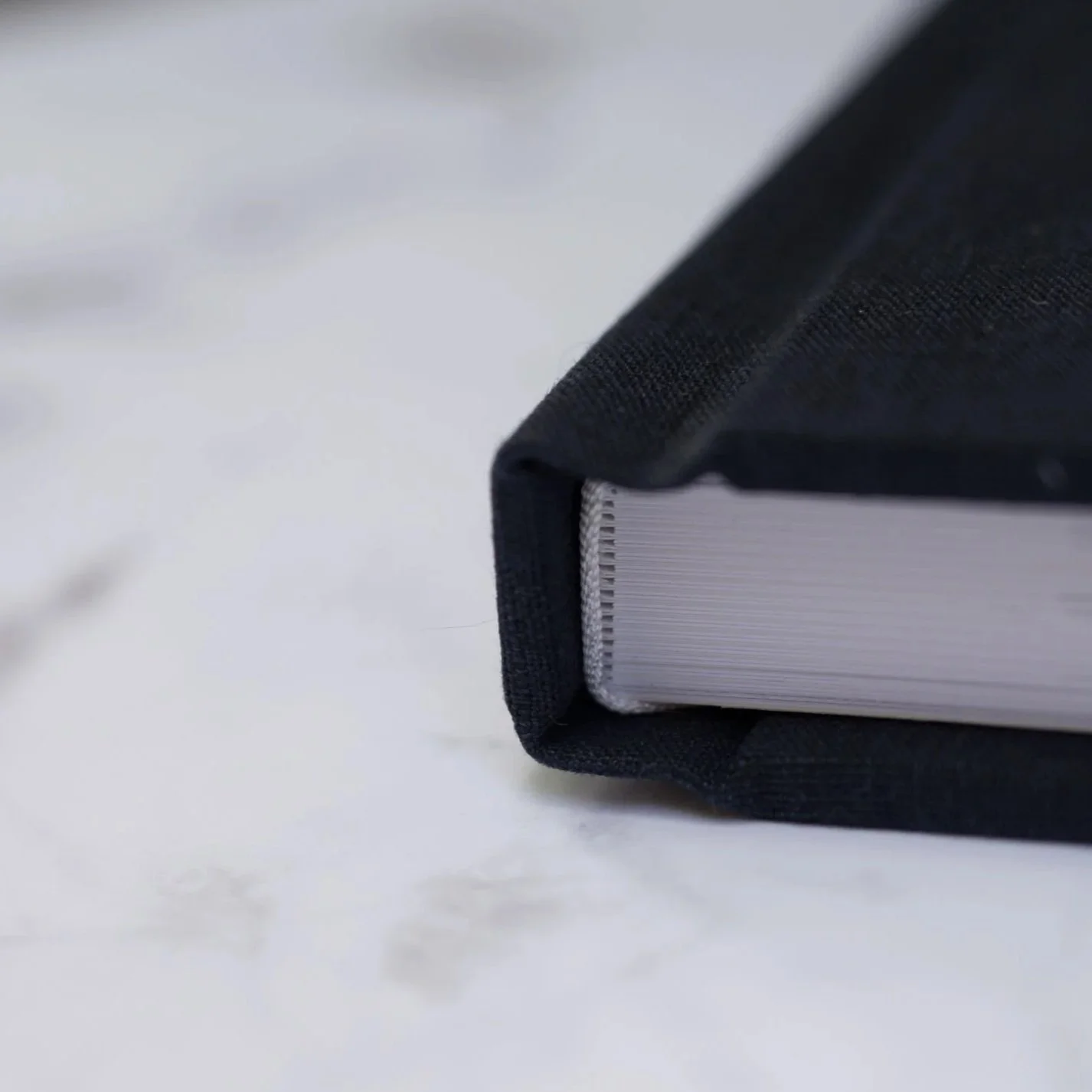 Spine of a fine art photo album with navy linen cover on marble surface