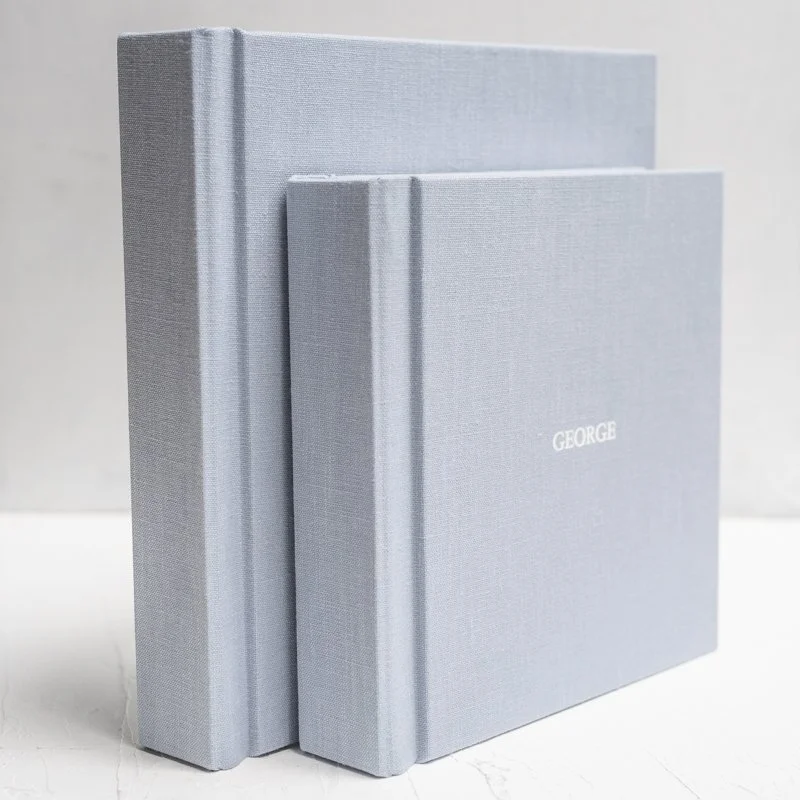 Two light blue linen photo albums with elegant script debossing on the cover, styled as a luxury custom newborn photo album keepsake.