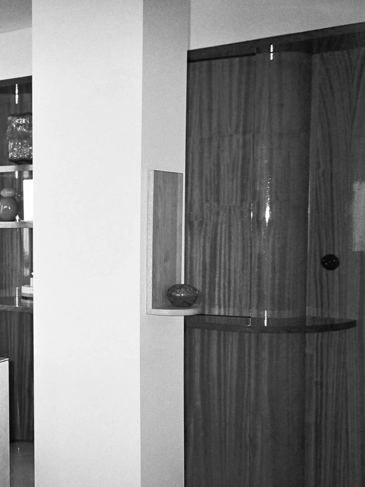 Interior of a home with a wooden and glass display cabinet, some decorative plates or vases, and a part of a white wall.