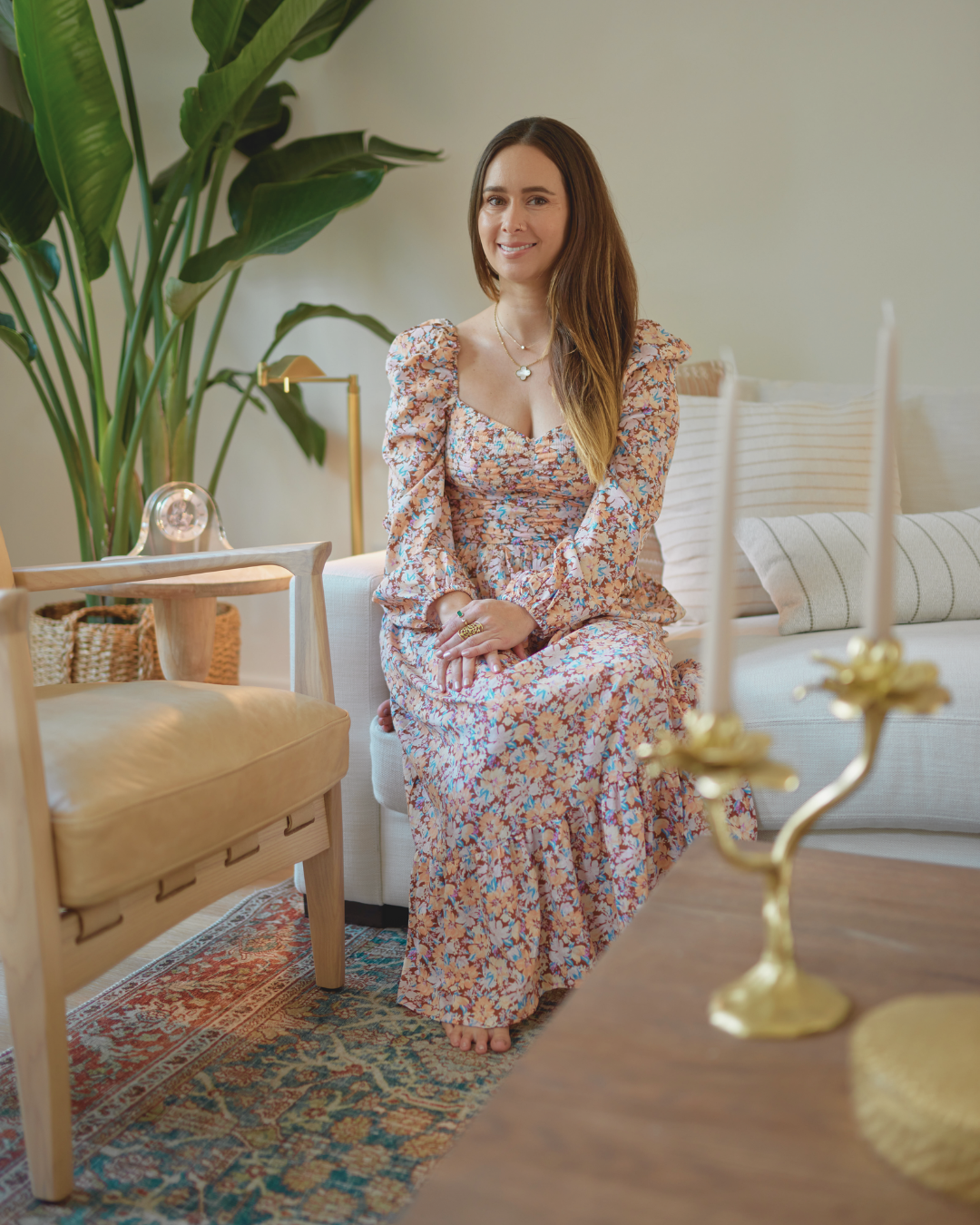 Paula sitting on a sofa between gold candlesticks and a tall plant