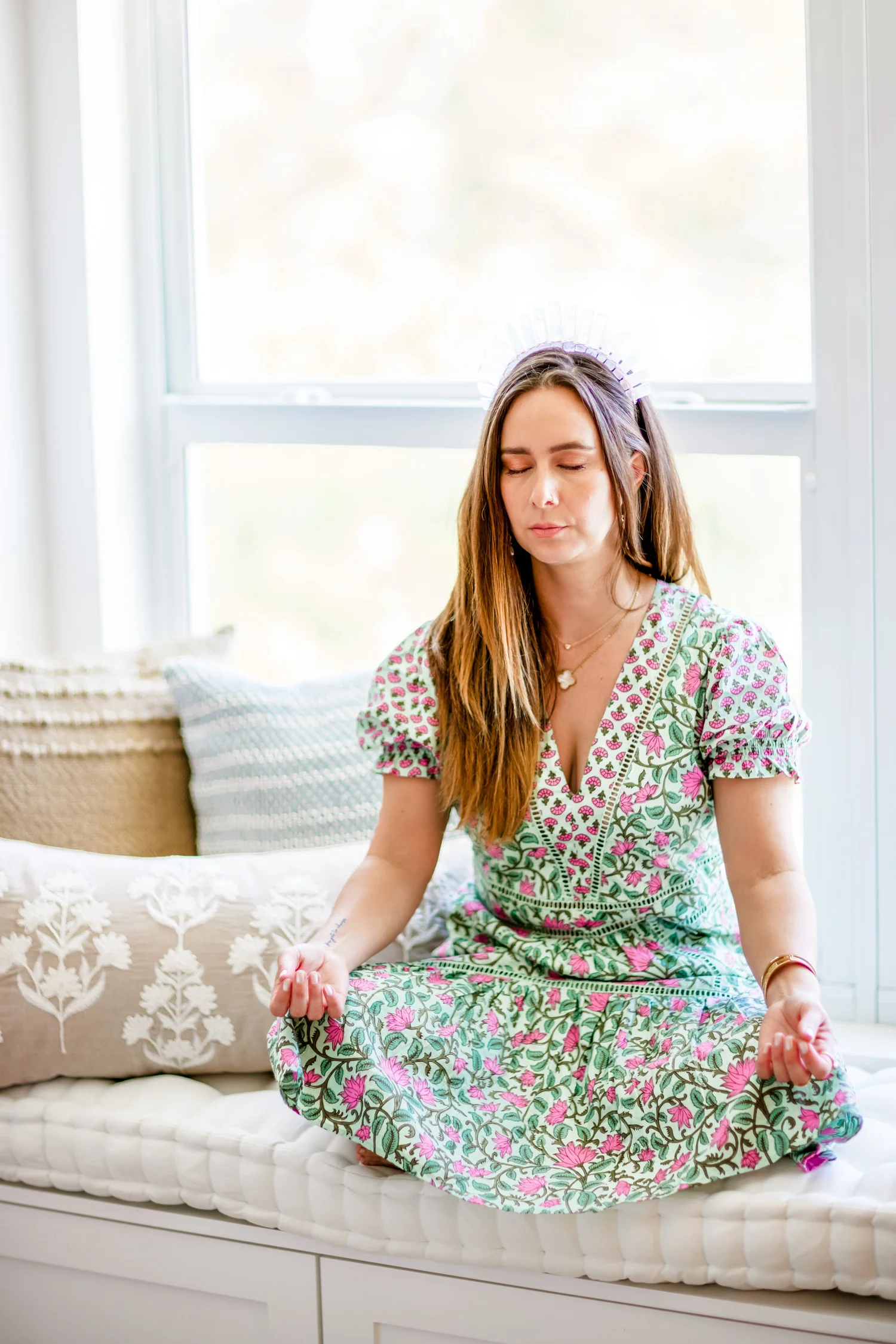 Paula sitting cross-legged on a window seat with her eyes closed