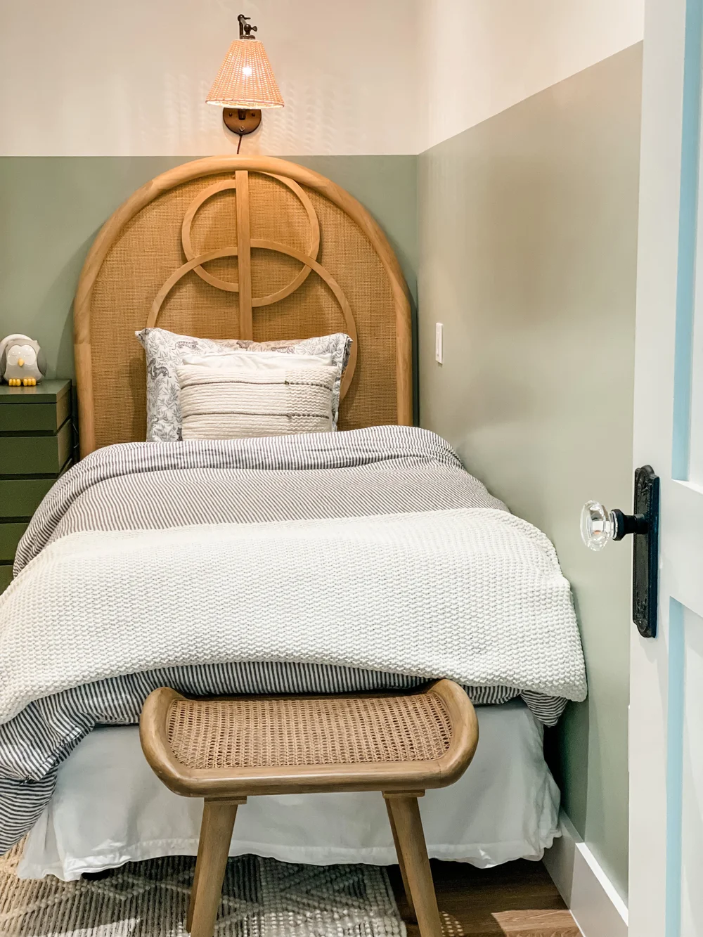 A bedroom with an arched rattan headboard and soft green walls