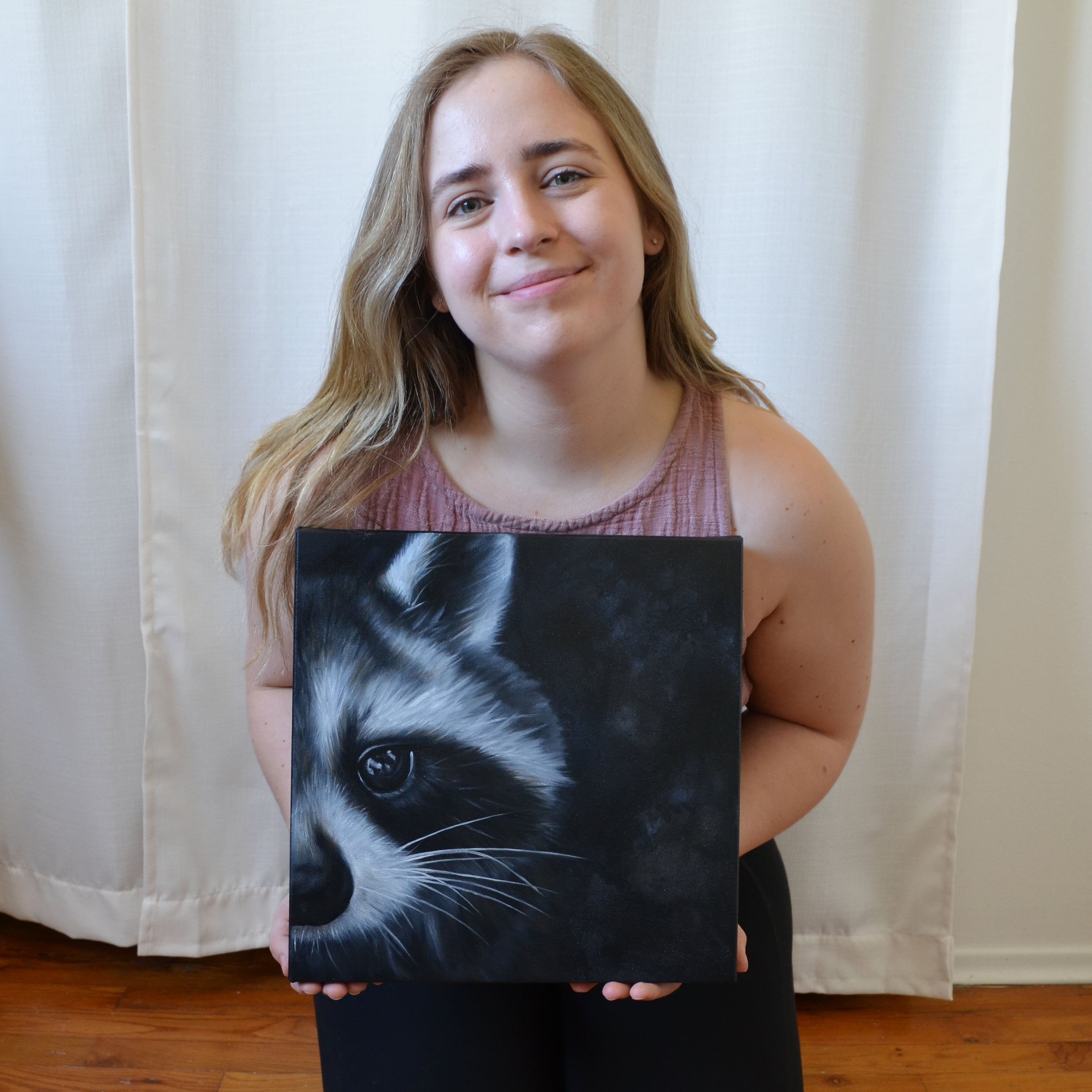 female artist holding an oil painting of a raccoon