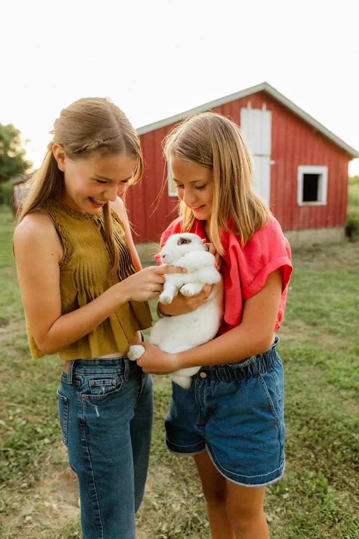  two girls holding a bunny in front of a barn 