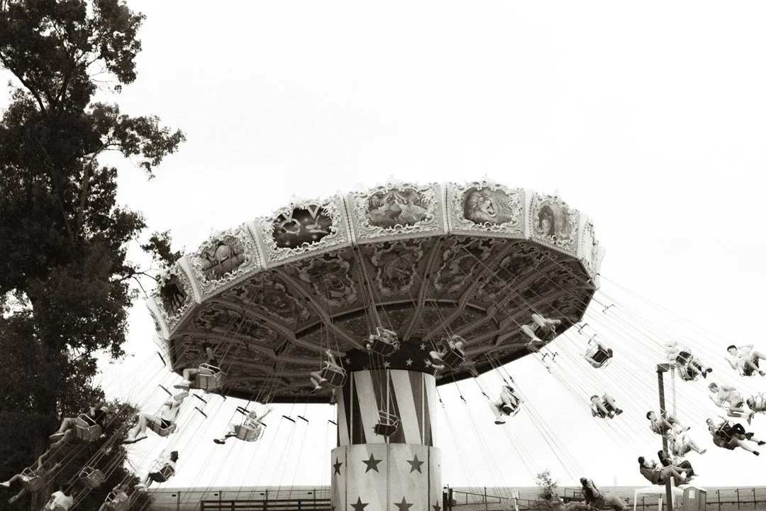 A vintage swing ride at an amusement park with many children riding it, black and white photo.