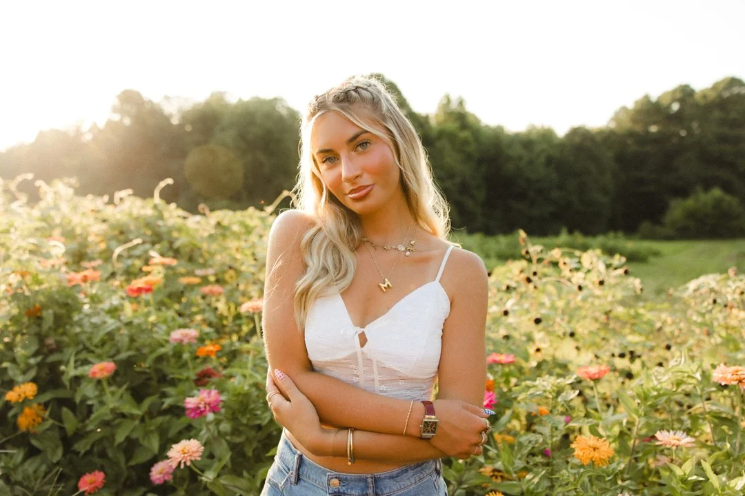A young woman with long blonde hair standing in a flower field during sunset.