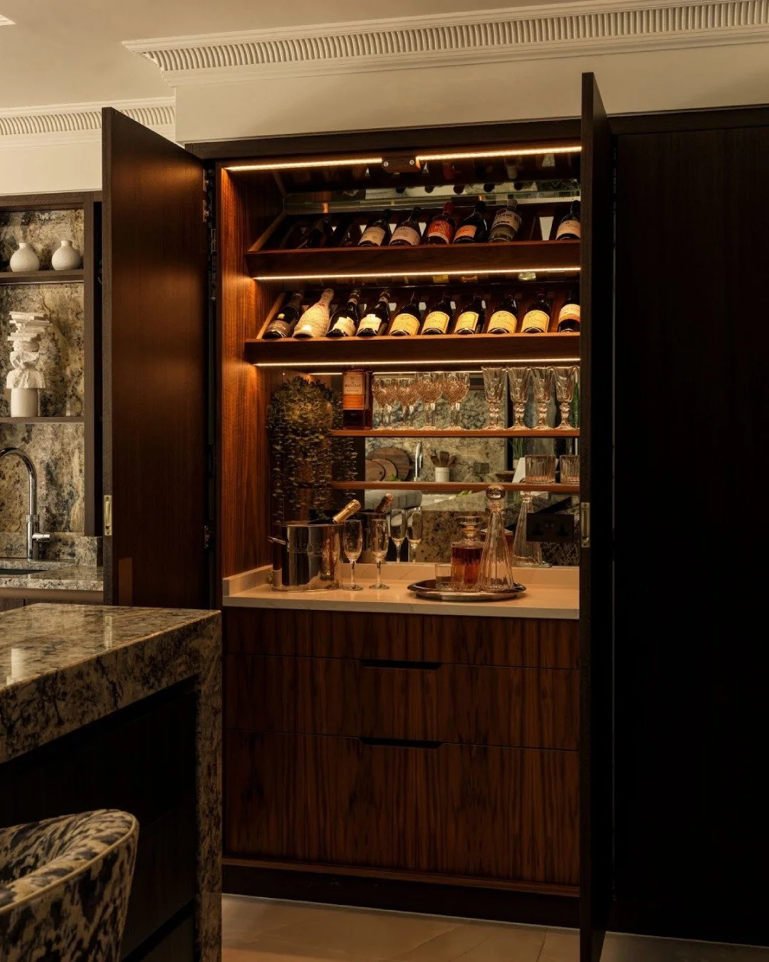 This bar opens to a thoughtful arrangement of shelving, wine storage and softly lit surfaces. Bottles sit at the top, glassware lines the back, and everything stands out without ever feeling on show. Hidden until the moment calls for it, the space qu