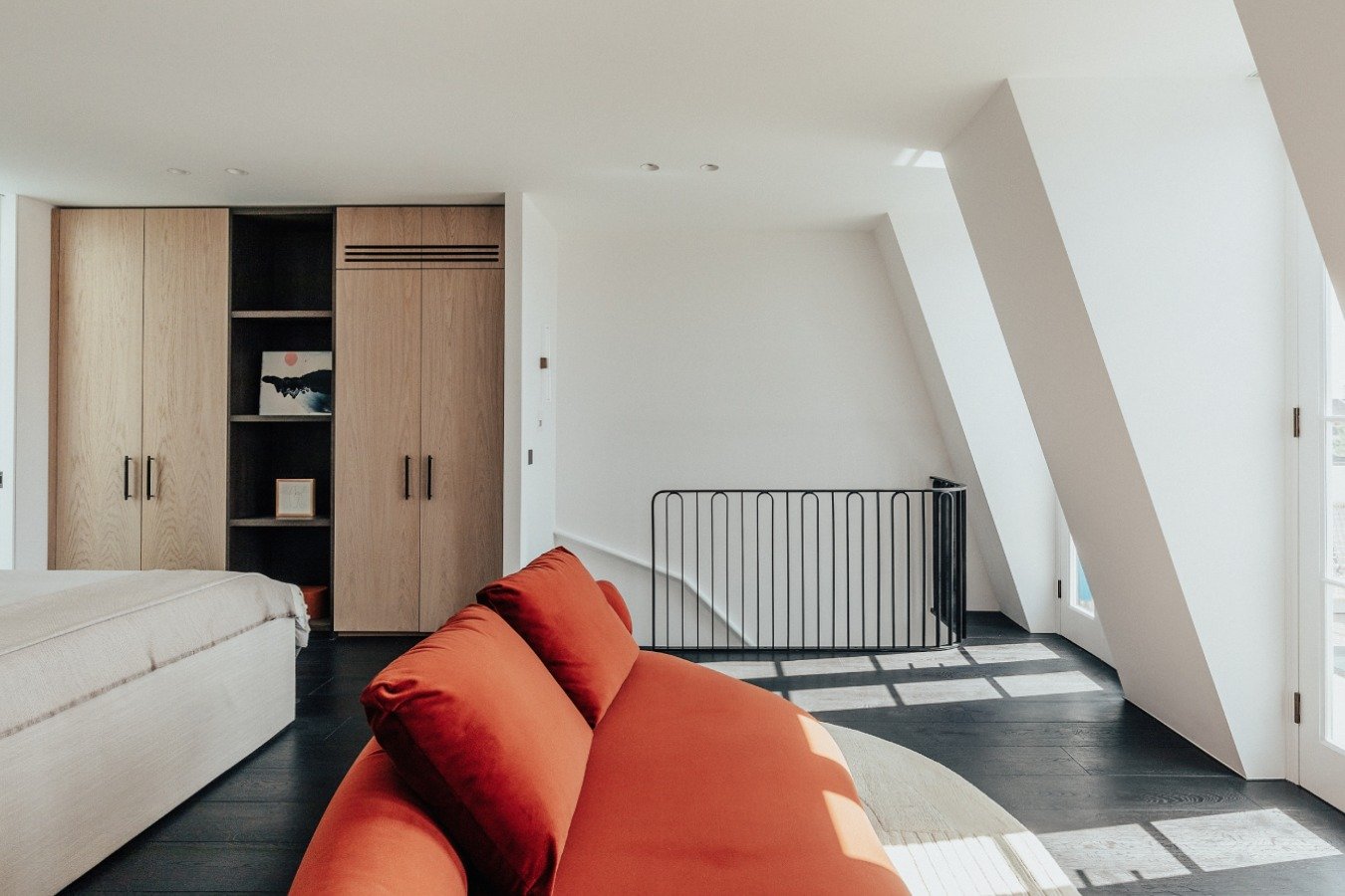 In this main bedroom, wardrobes sit on either side of the bed, combining long and short hangings with central display shelving, softly lit as doors open in the evening. The kitchen follows with crown-cut oak cabinetry, pocket doors concealing applian
