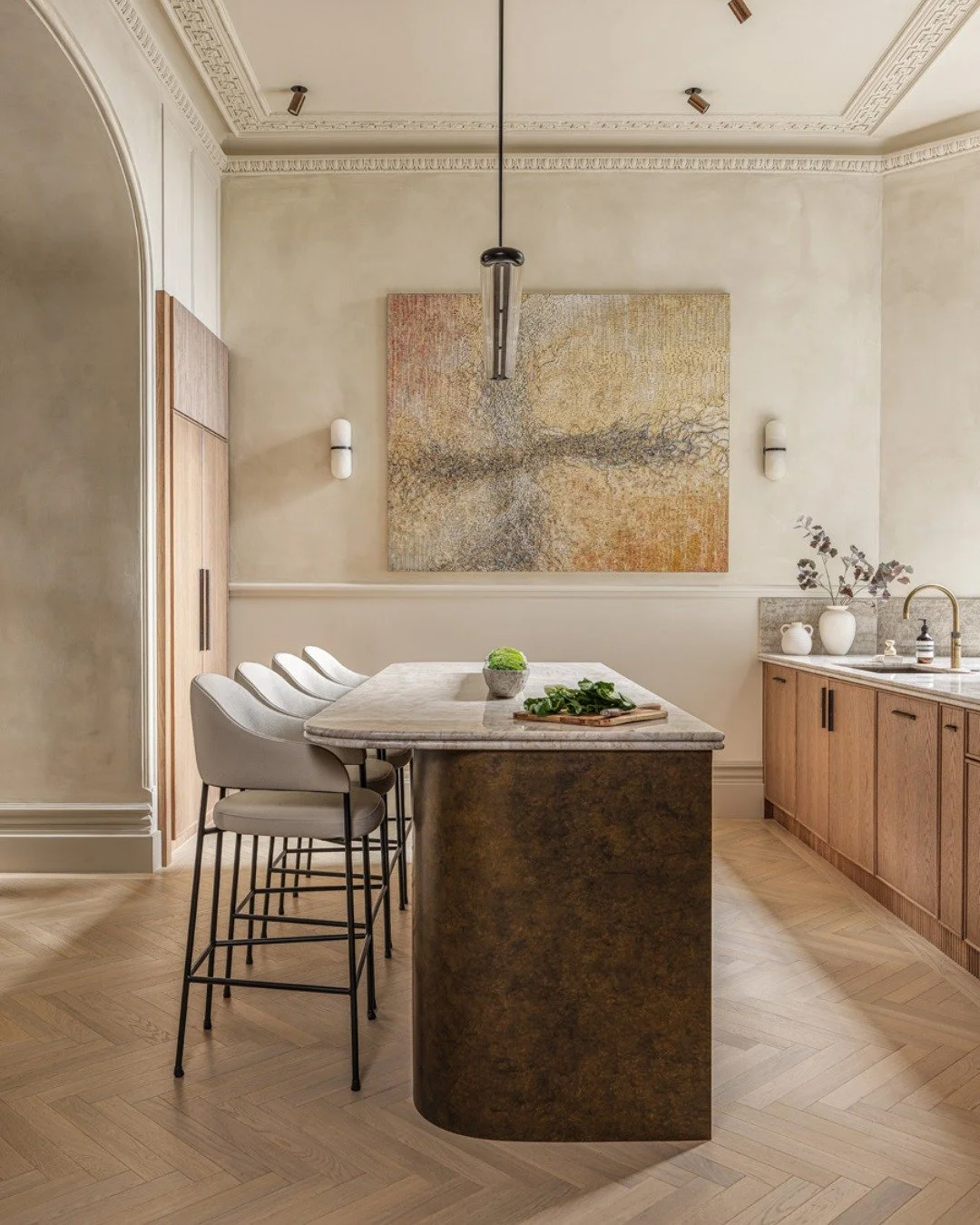 The curved antique brass base gives this island its character, topped with beautiful Taj Mahal quartzite that offers a generous surface for whatever the day brings. Stools line up on one side, creating a clear seating space, while the remaining space