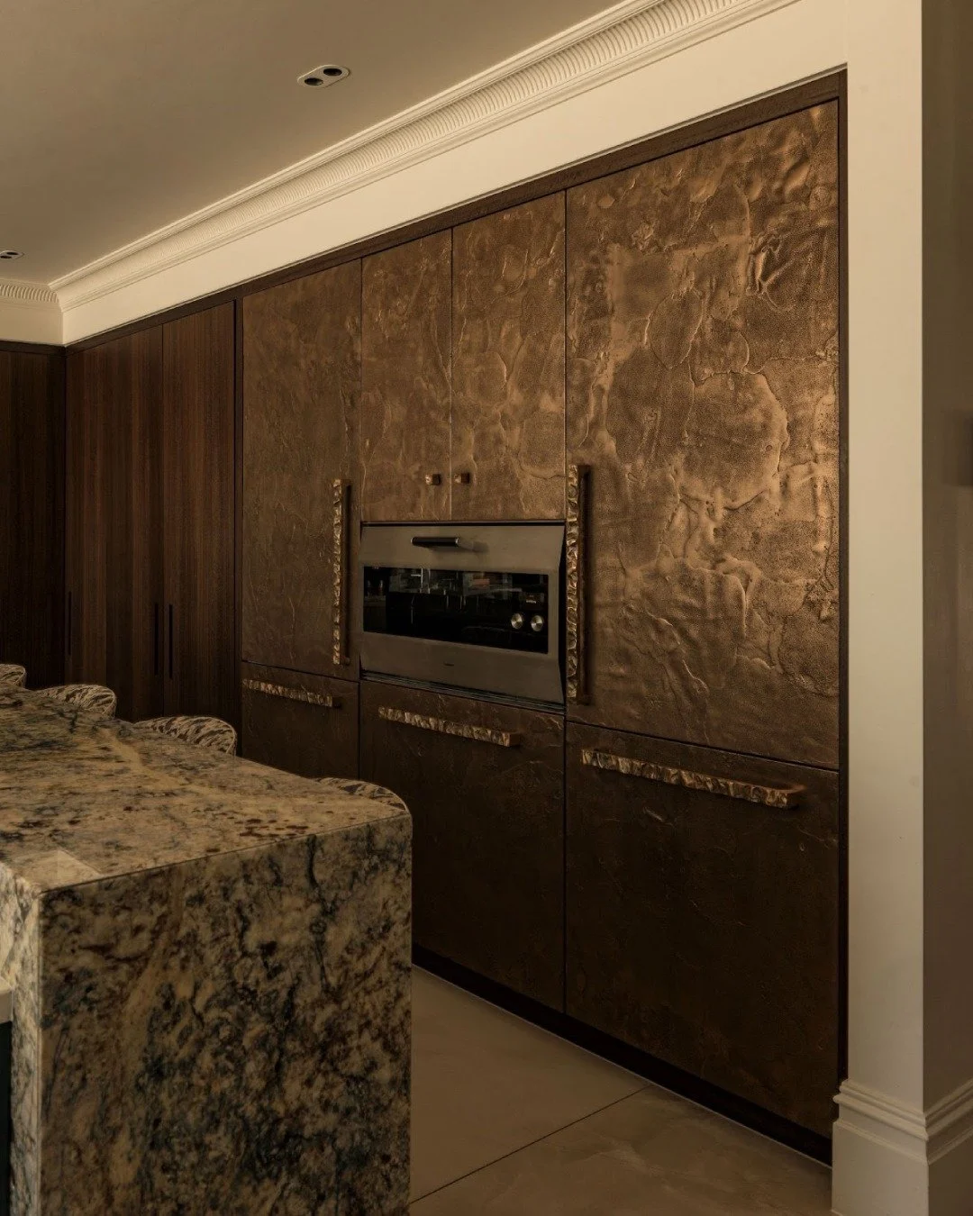 This side of the kitchen holds the quieter details that give the room its unique character. Ragged Shagreen bronze panels introduce texture and depth, framed with liquid metal edges that give each section a refined finish. Appliances are integrated w