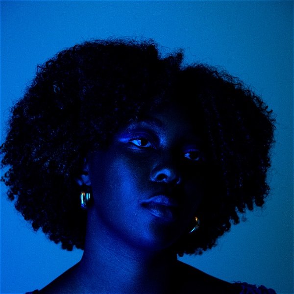 Blue-lit black woman with gold earrings stares wistfully off camera