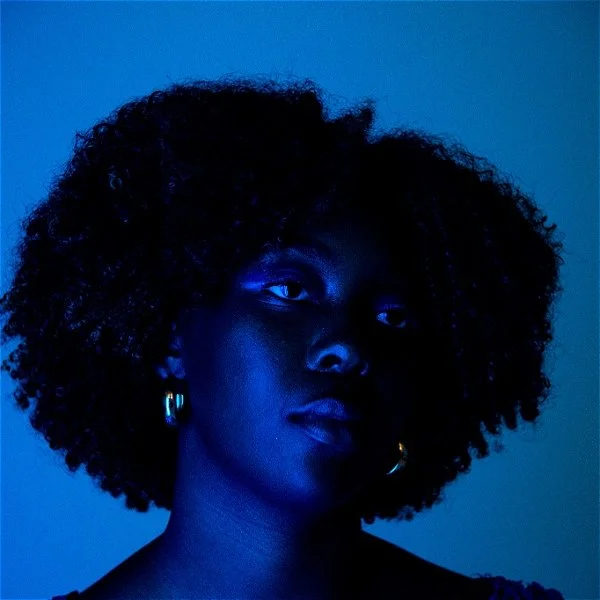 Blue-lit black woman with gold earrings stares wistfully off camera