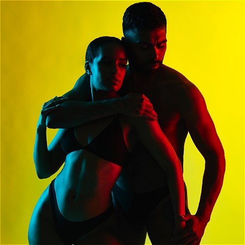 Two dancers embrace lit in blue on one side and red on the other, before a perfectly yellow background