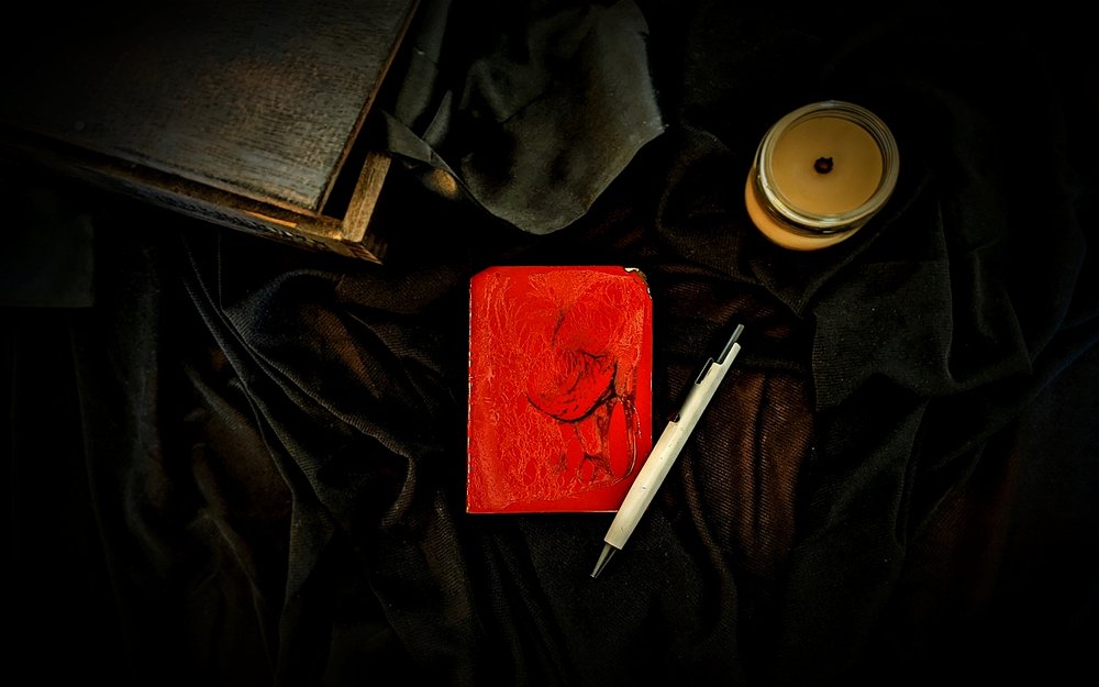 A closed red notebook and whtie pen sit on black velvet cloth