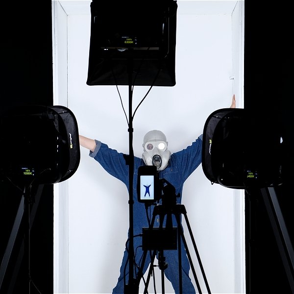 Someone in denim overalls and a gas mask does jumping jacks in front of a camera in a photo studio, in front of a white backdrop